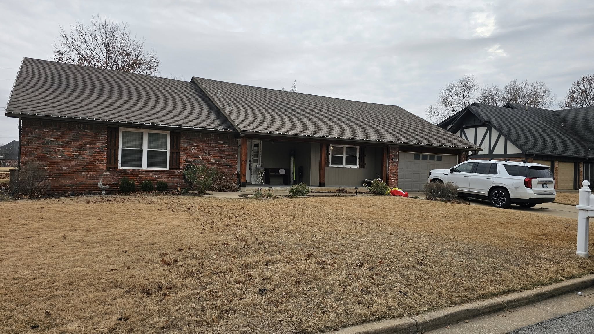 A white SUV is parked in the driveway of a brick house on a cloudy day.