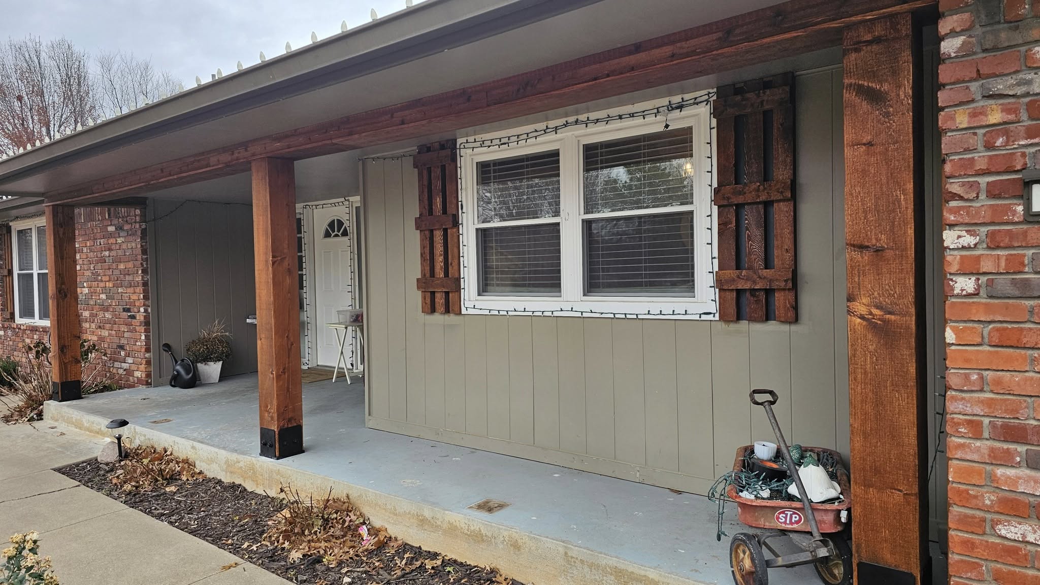 A house porch with wooden posts, shutters, and a wagon filled with Christmas lights.