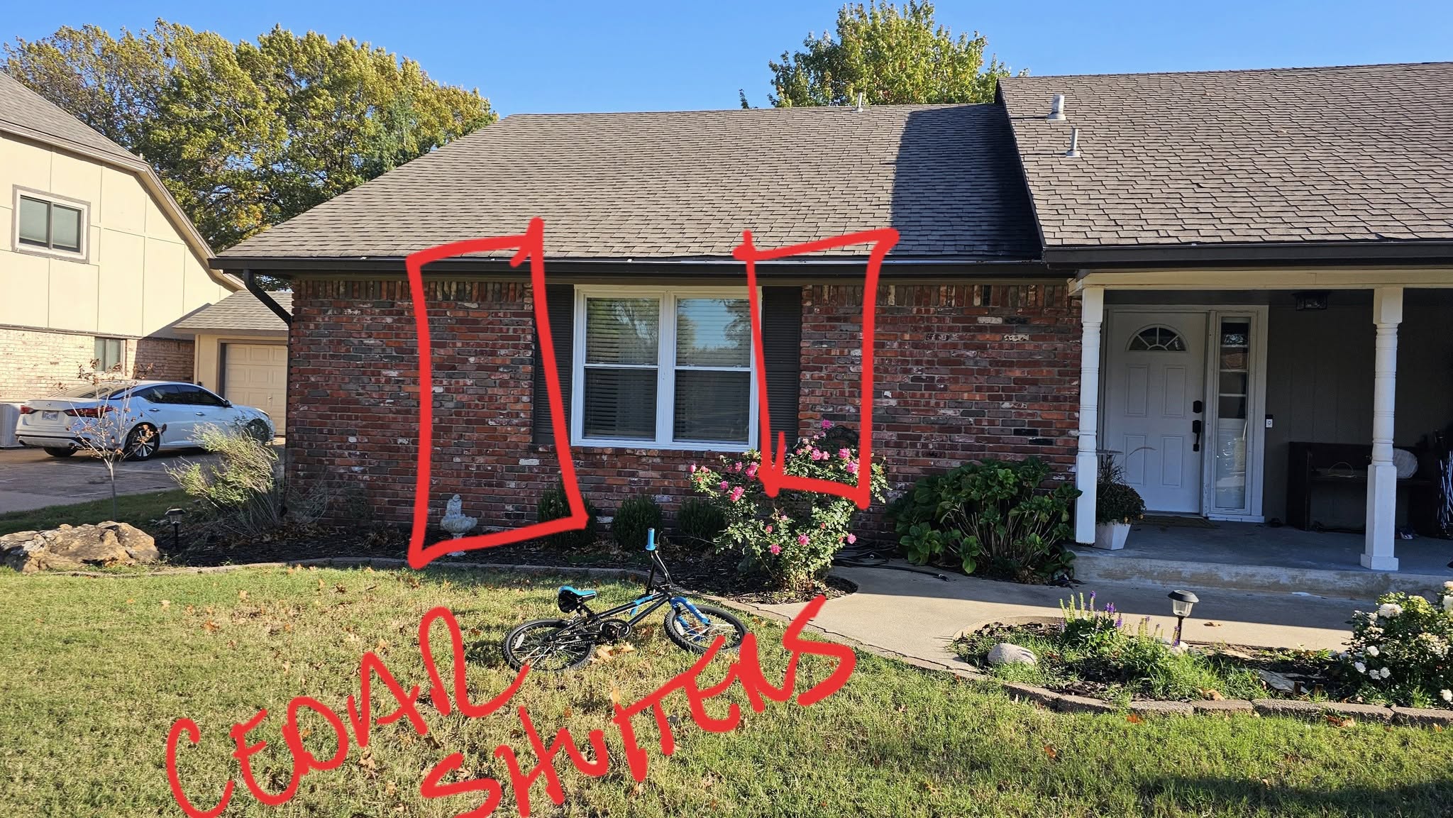 A house with red brick, a window, and a bicycle in the yard.
