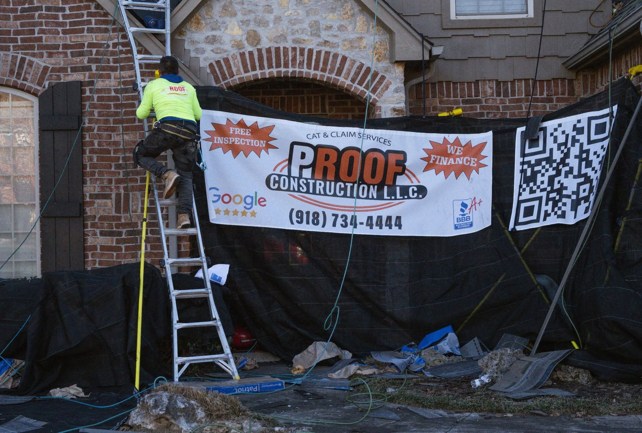 A roofer climbs a ladder in front of a banner for Proof Construction LLC.