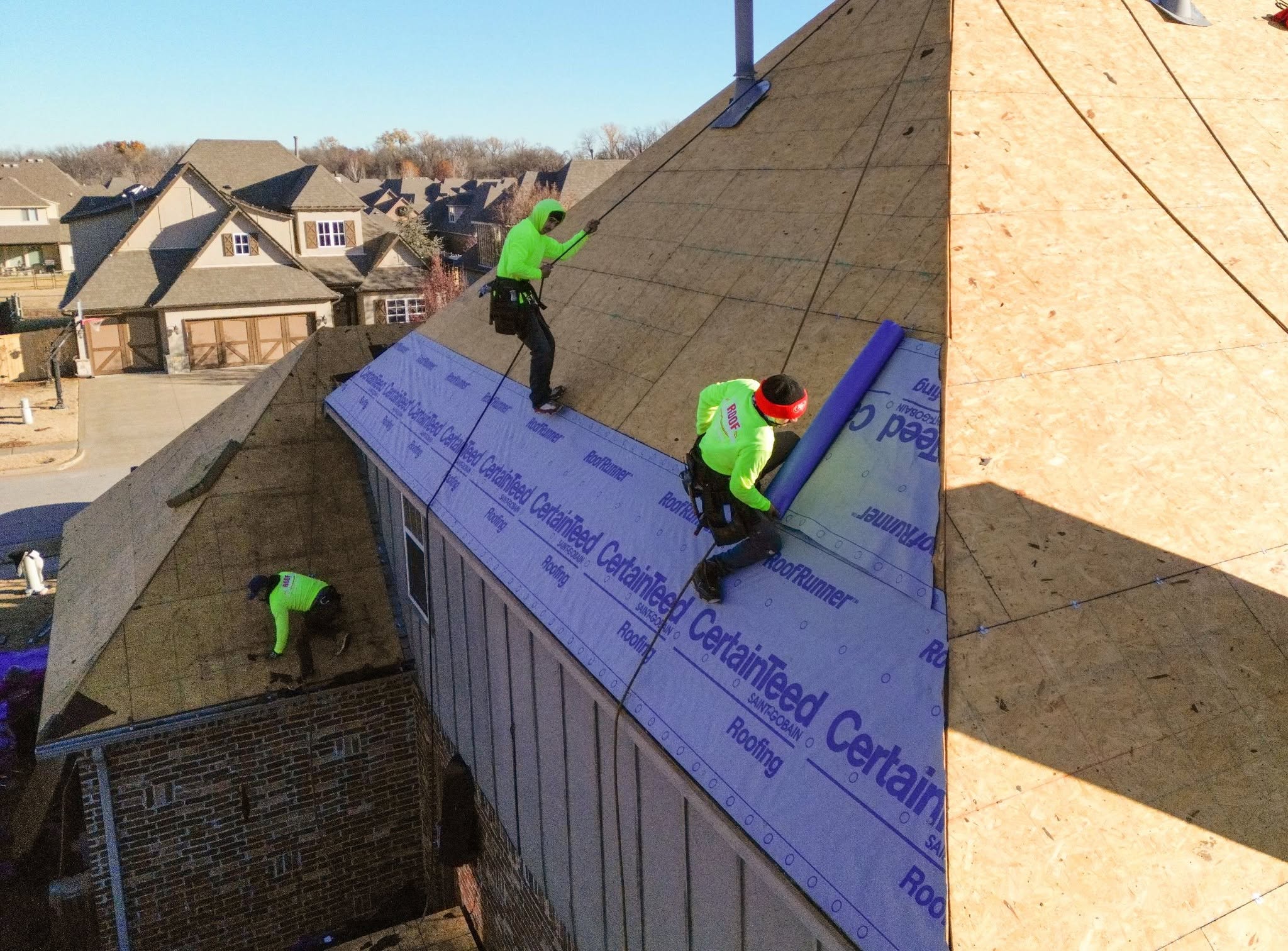 Roofers work on a house roof, installing underlayment.