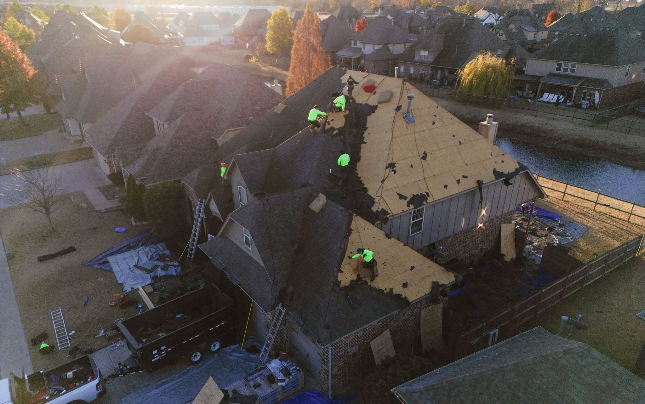 Roofers work on a damaged house in a suburban neighborhood.