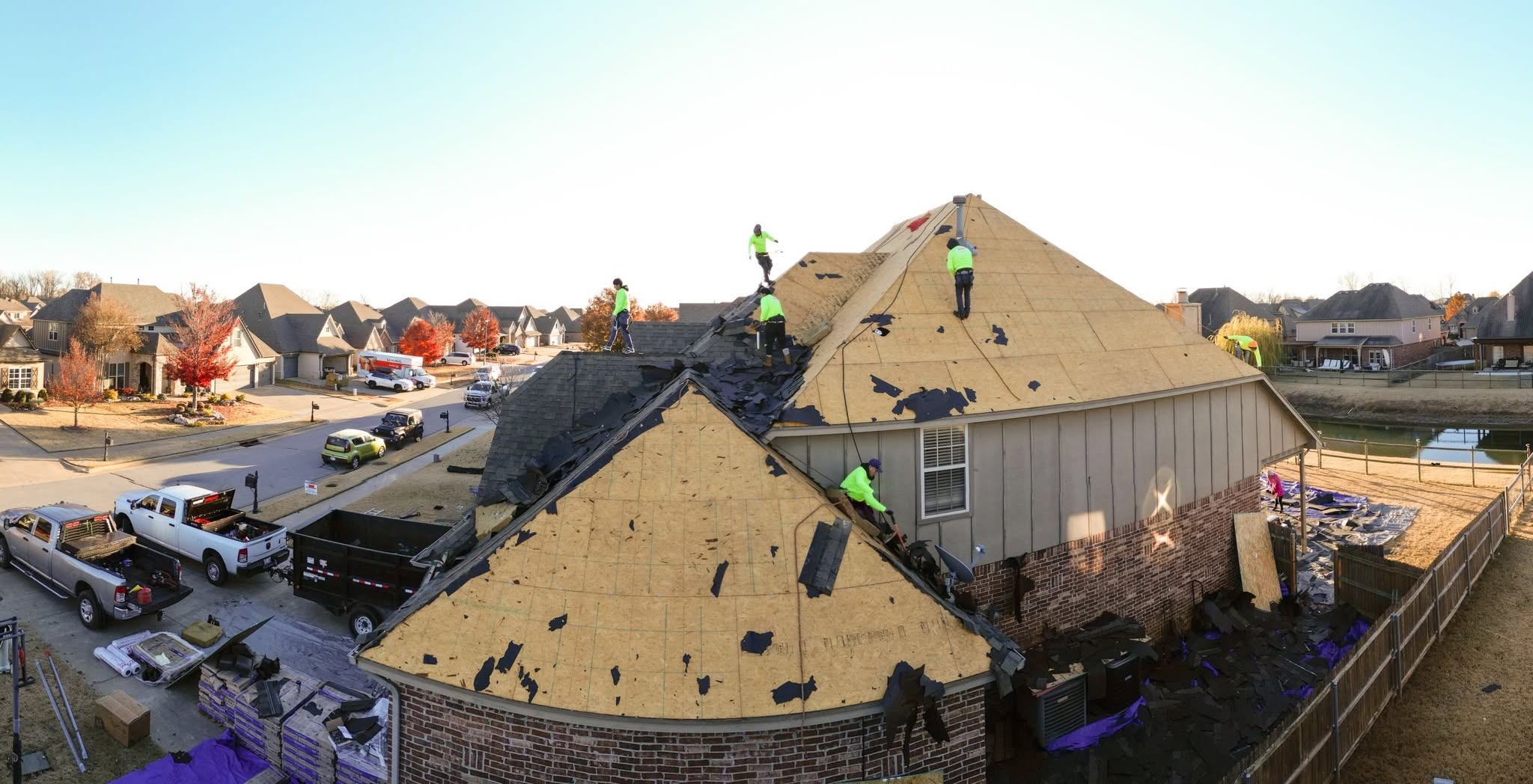 Roofers on a damaged house in a suburban neighborhood.
