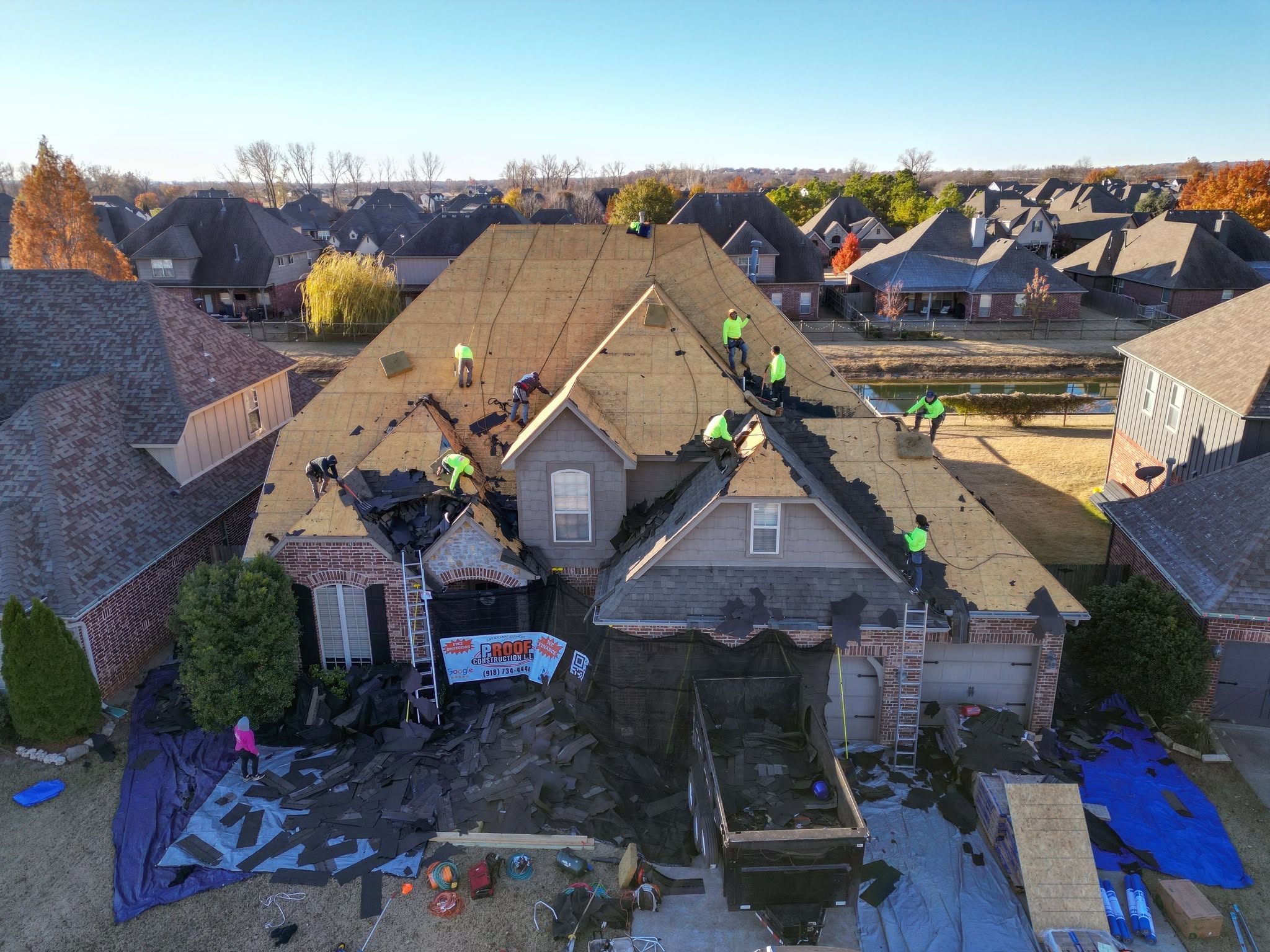 Roofers work on a house in a suburban neighborhood, removing old shingles.