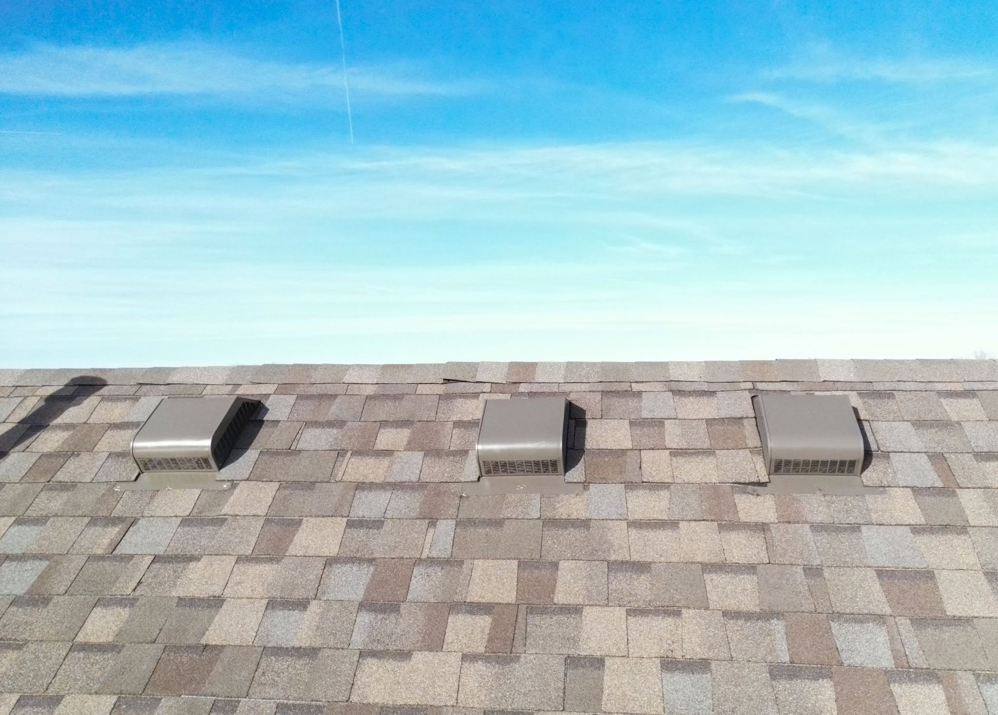 Three roof vents are visible on a shingled roof under a bright blue sky.