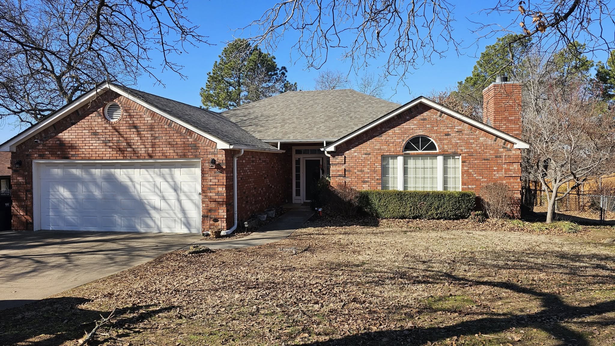 A red brick house with a white garage door sits on a sunny day.