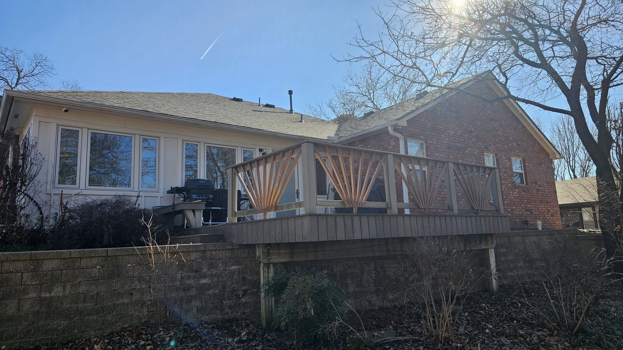 A brick and white house with a deck and grill is shown outdoors on a sunny day.