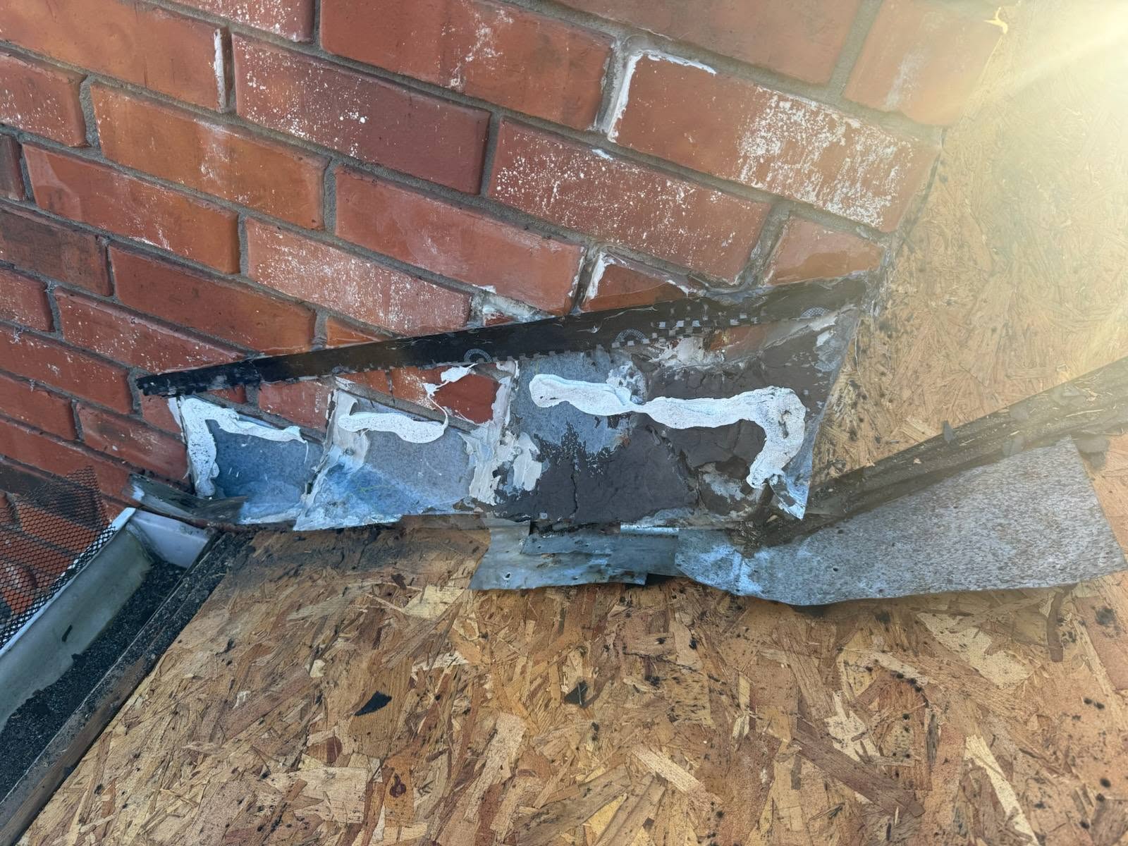 This image shows a close-up of a brick wall with flashing and sealant, likely on a roof or exterior wall.