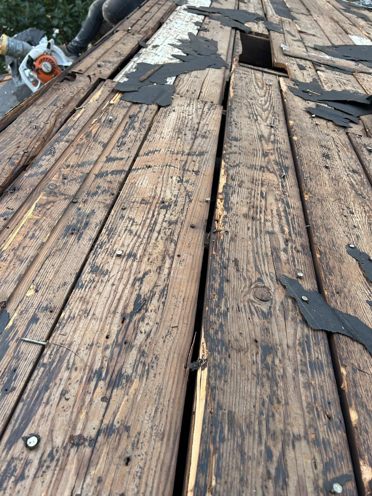 A roofer works on a damaged wooden roof with a circular saw.