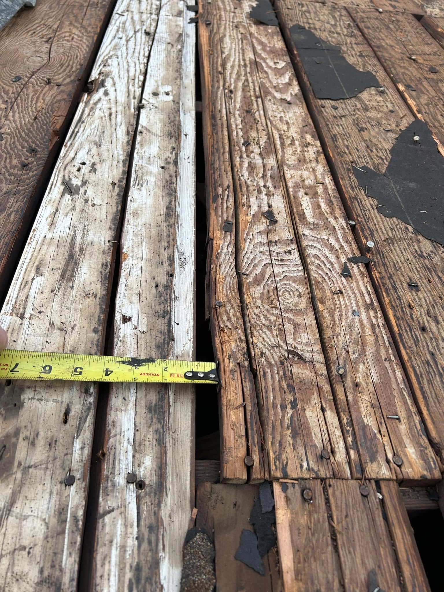 A close-up view of weathered wooden planks on a roof, with a tape measure indicating a gap.