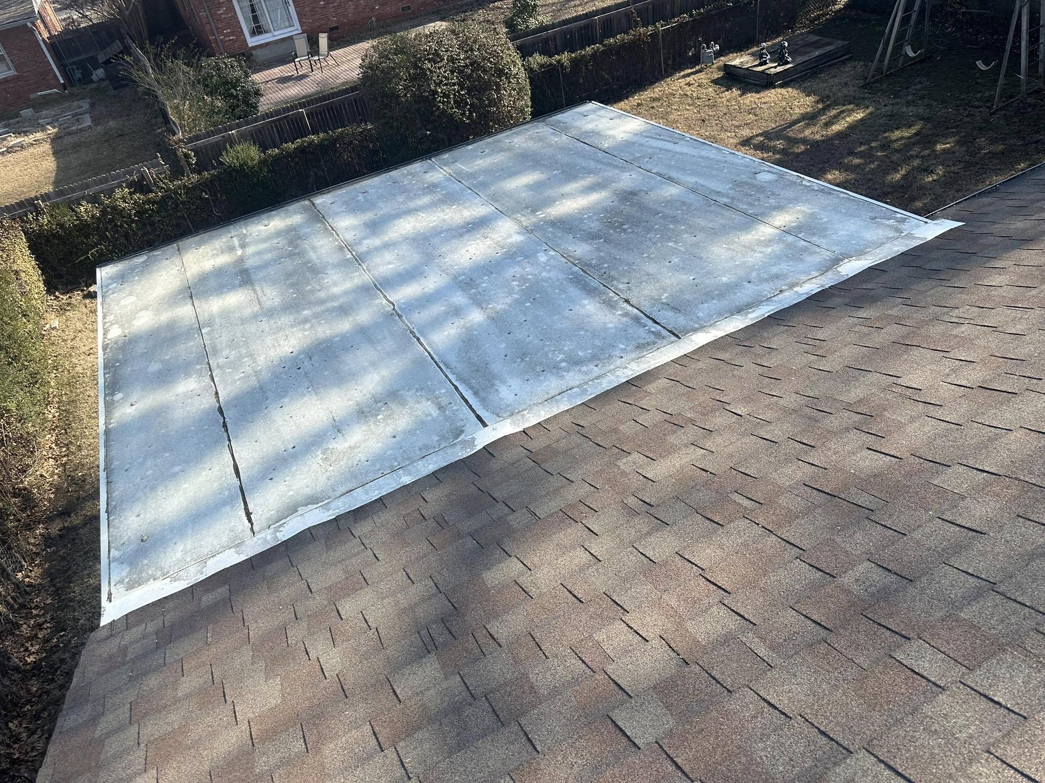 A flat roof section is installed over a sloped shingle roof in a backyard.