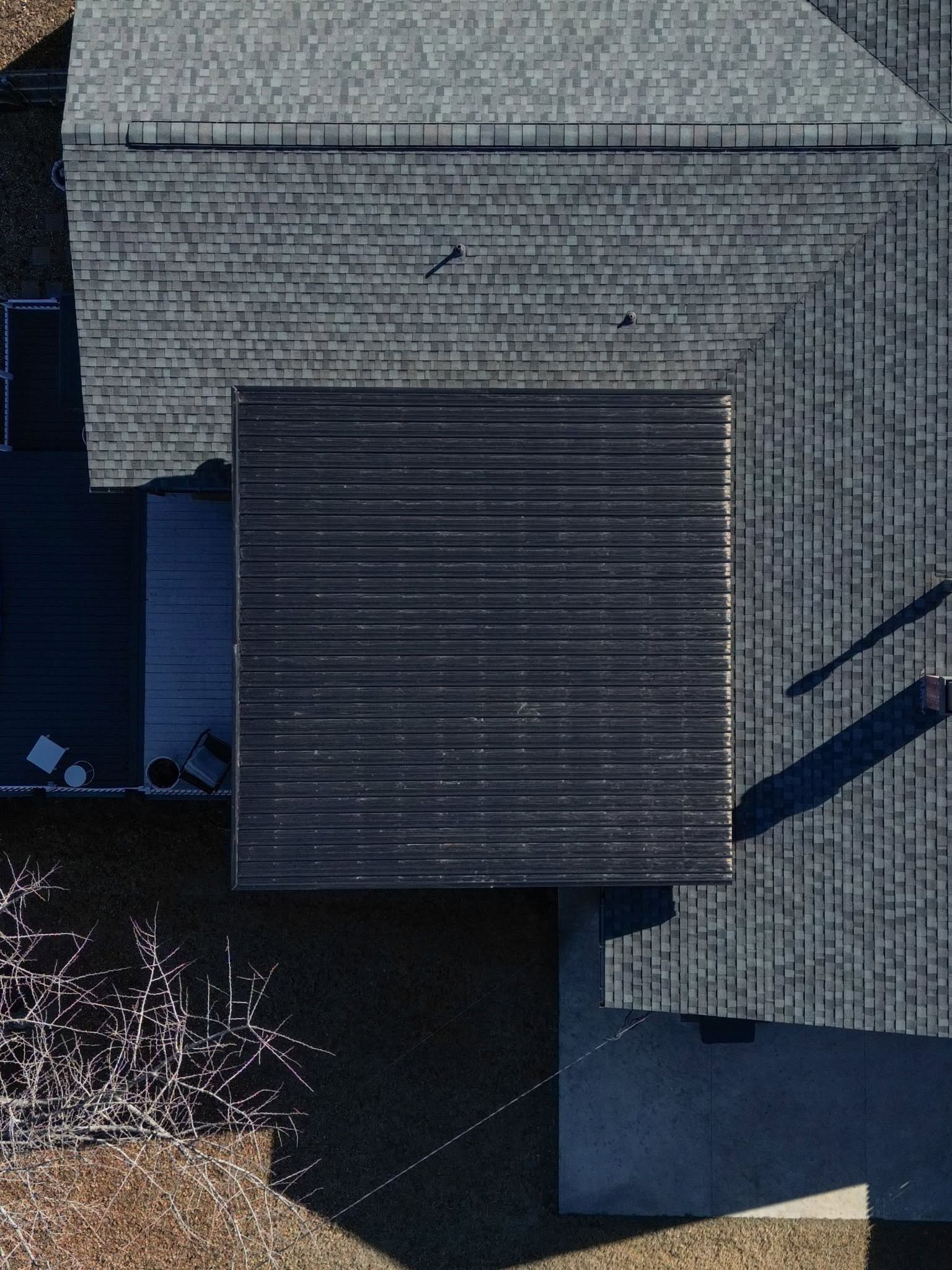 An aerial view of a dark-roofed house with a grey shingled roof and a concrete patio.