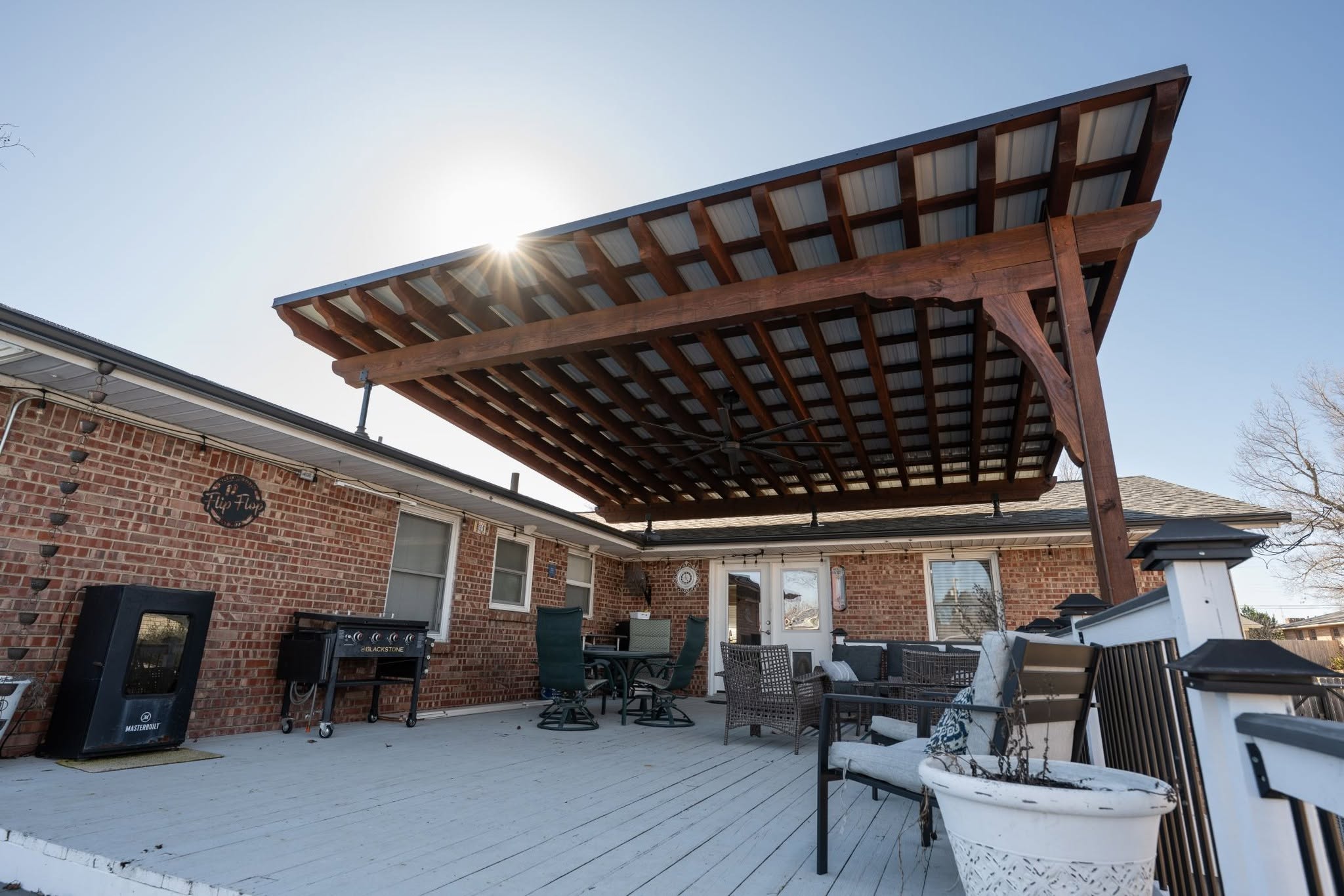 A covered patio with outdoor furniture and grills on a sunny day.