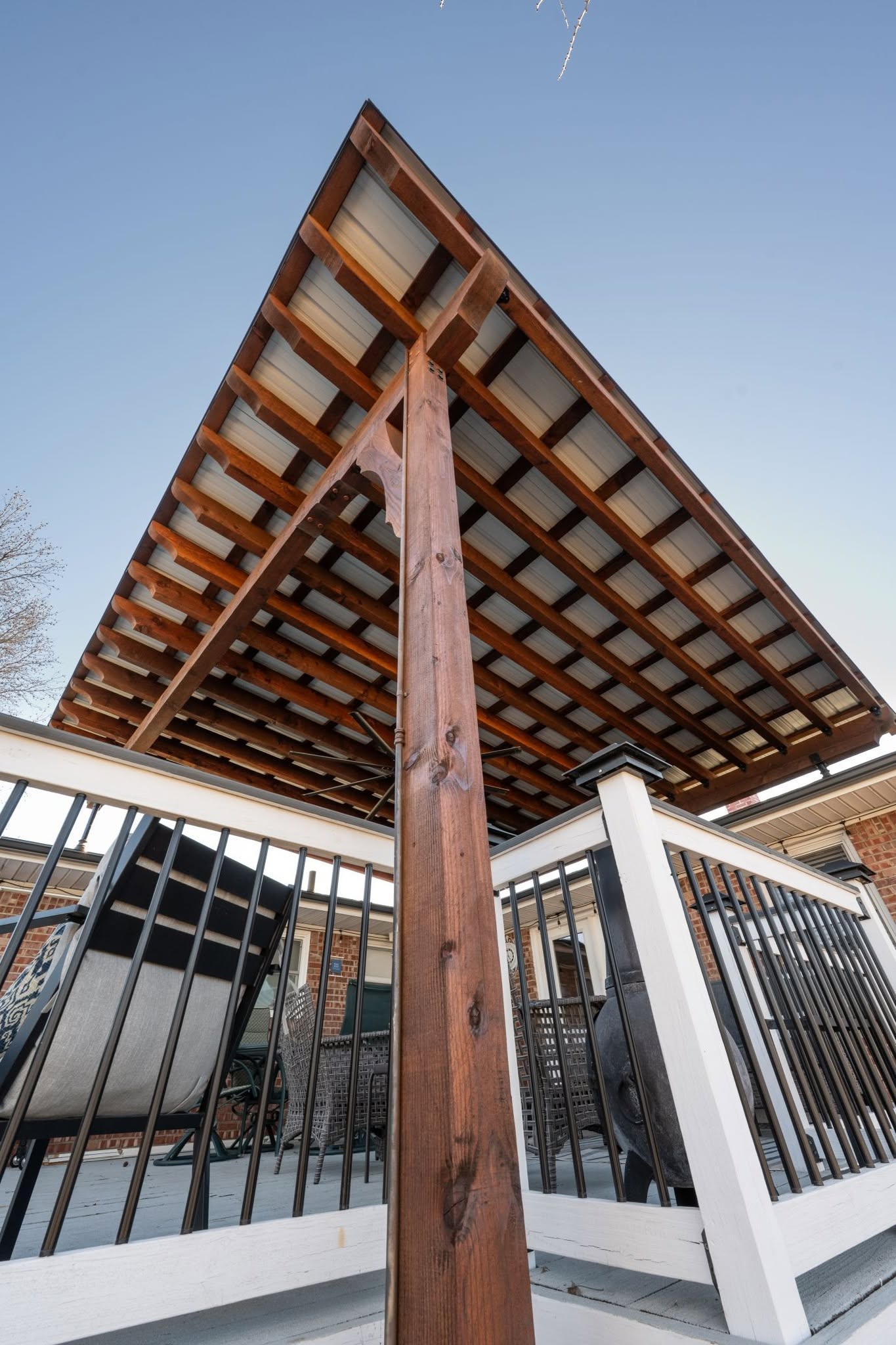 A wooden pergola covers a deck with outdoor furniture under a clear blue sky.