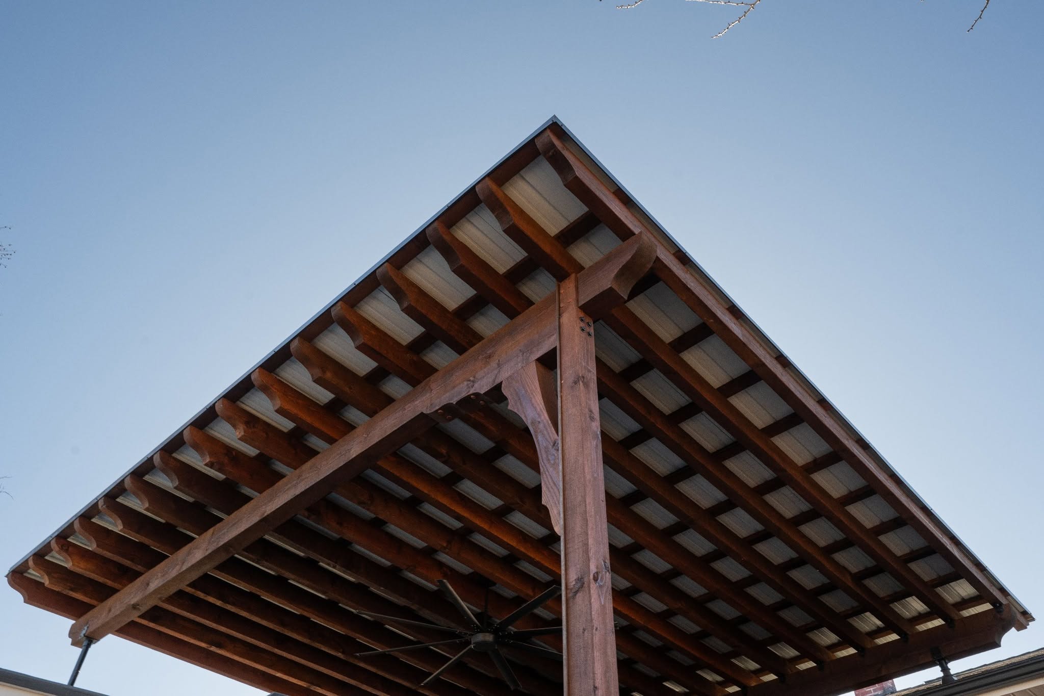 A wooden pergola with a metal roof is shown against a clear blue sky.
