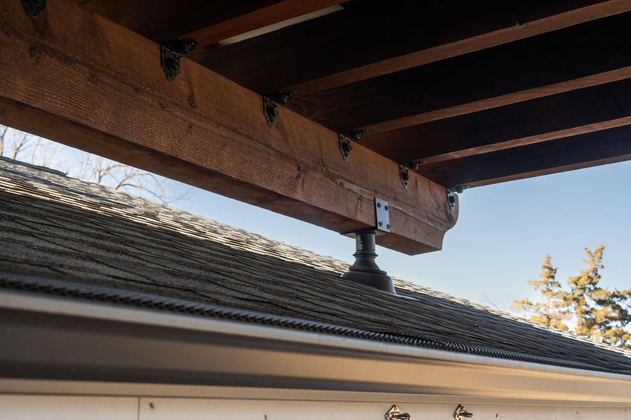 A wooden beam is supported by a decorative post on a shingled roof.