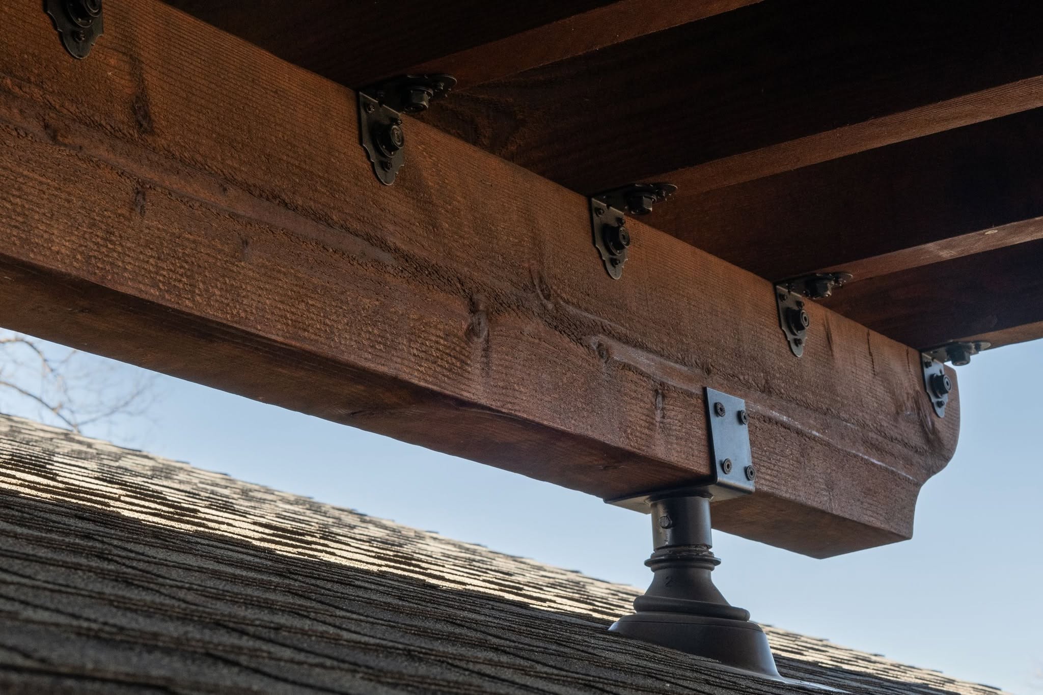 A wooden beam is supported by a decorative post on a shingled roof.