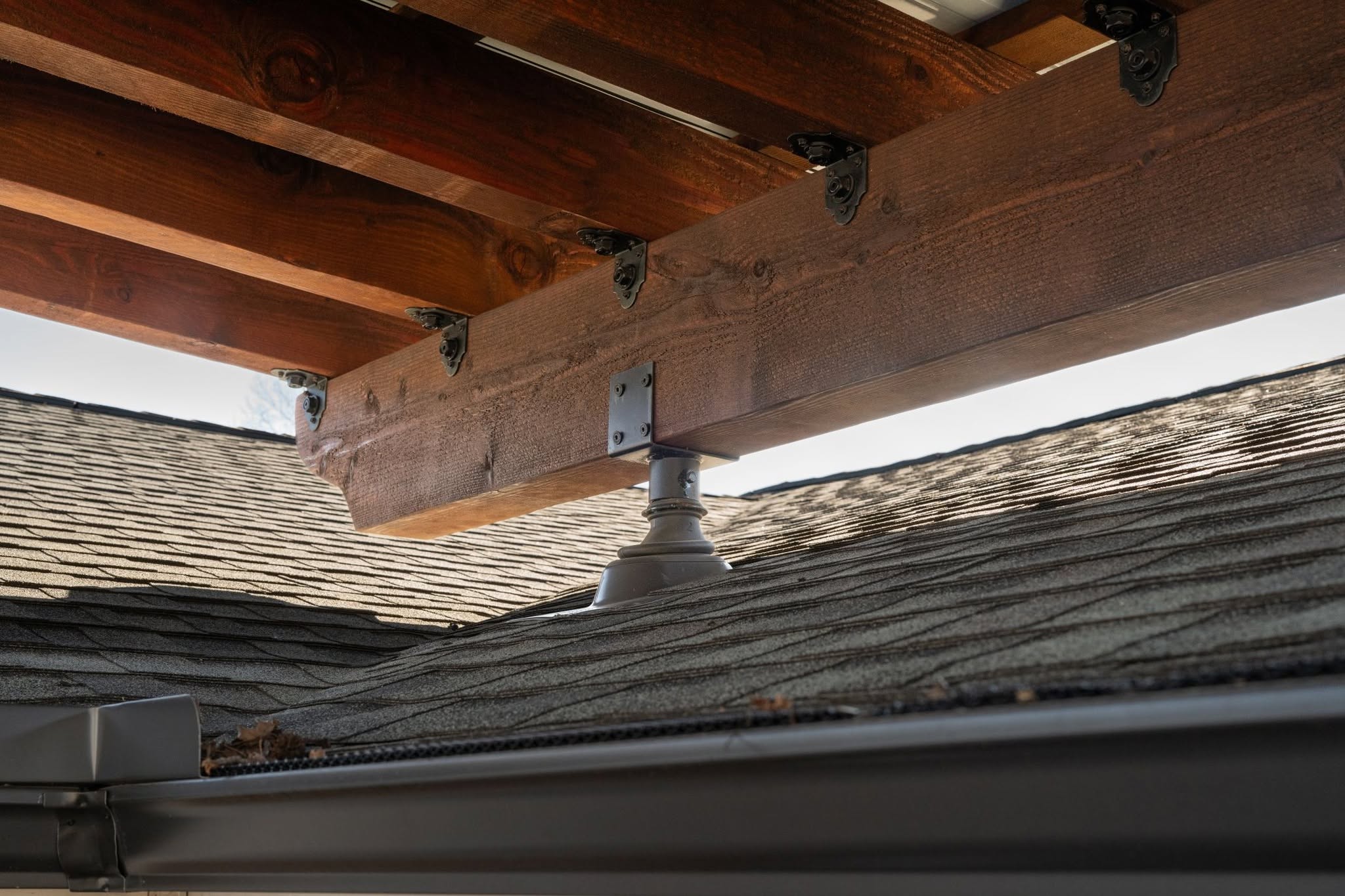 A wooden beam is supported by a metal bracket on a shingled roof.
