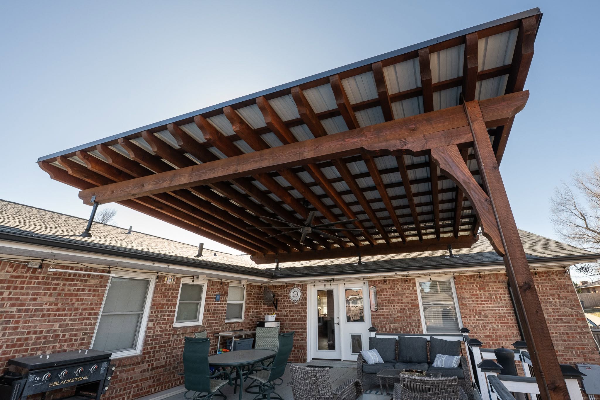 A covered patio with furniture and a fan is attached to a brick house.