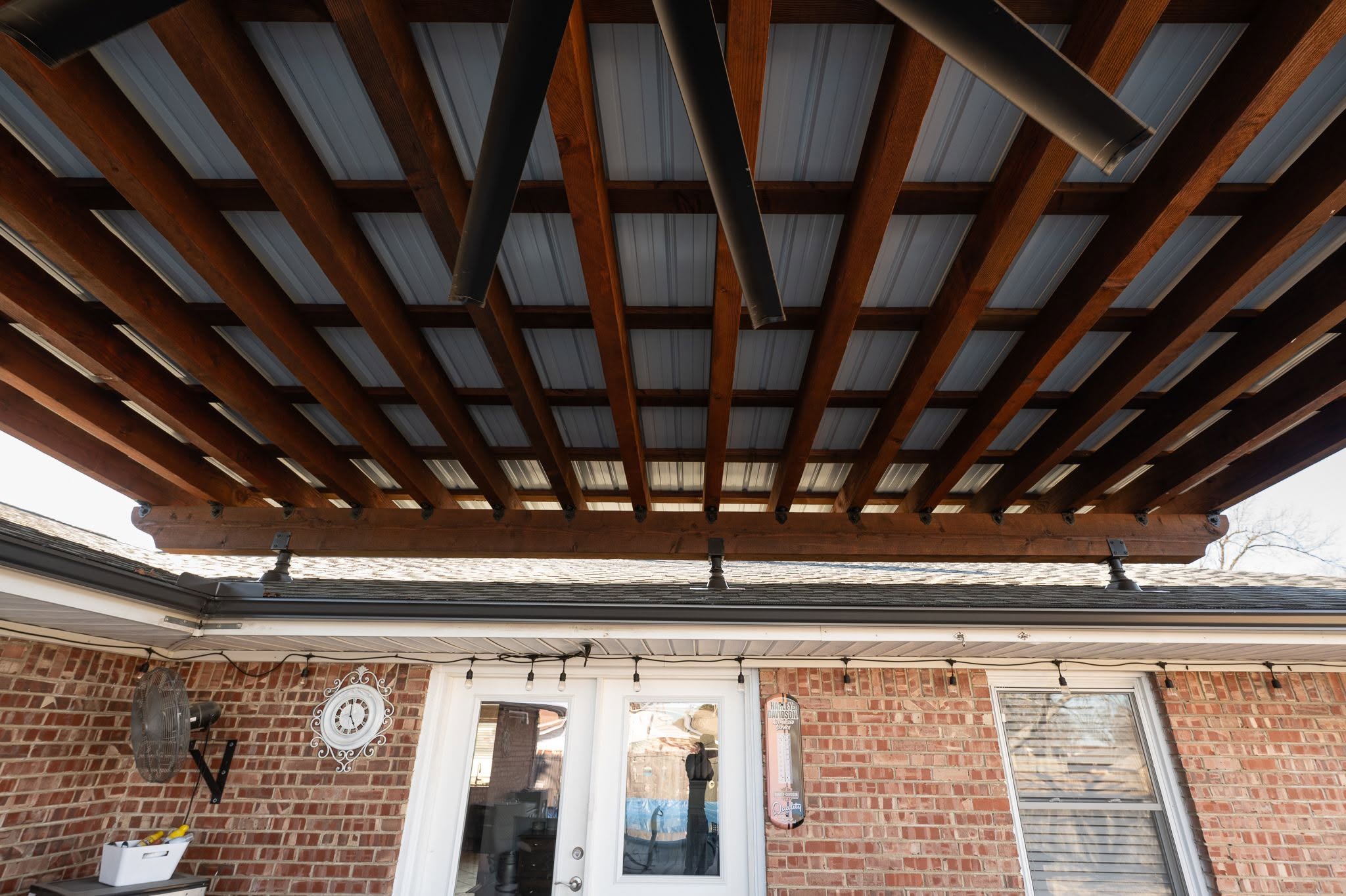 An outdoor patio with a wooden pergola, brick wall, and double doors.