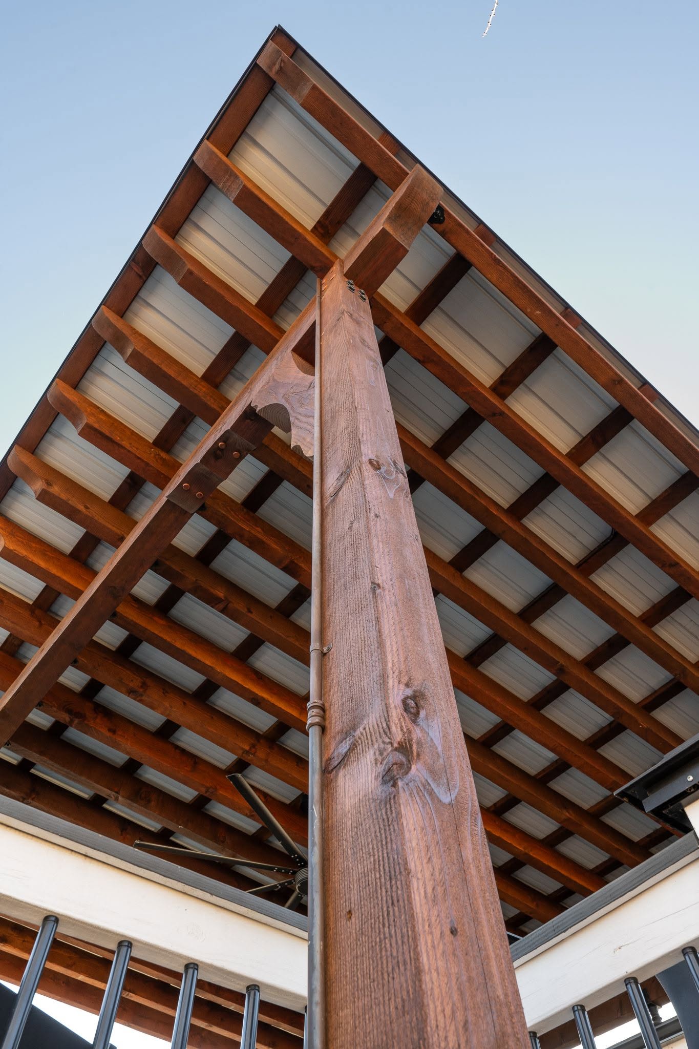 A wooden post supports a metal roof with visible rafters under a clear sky.