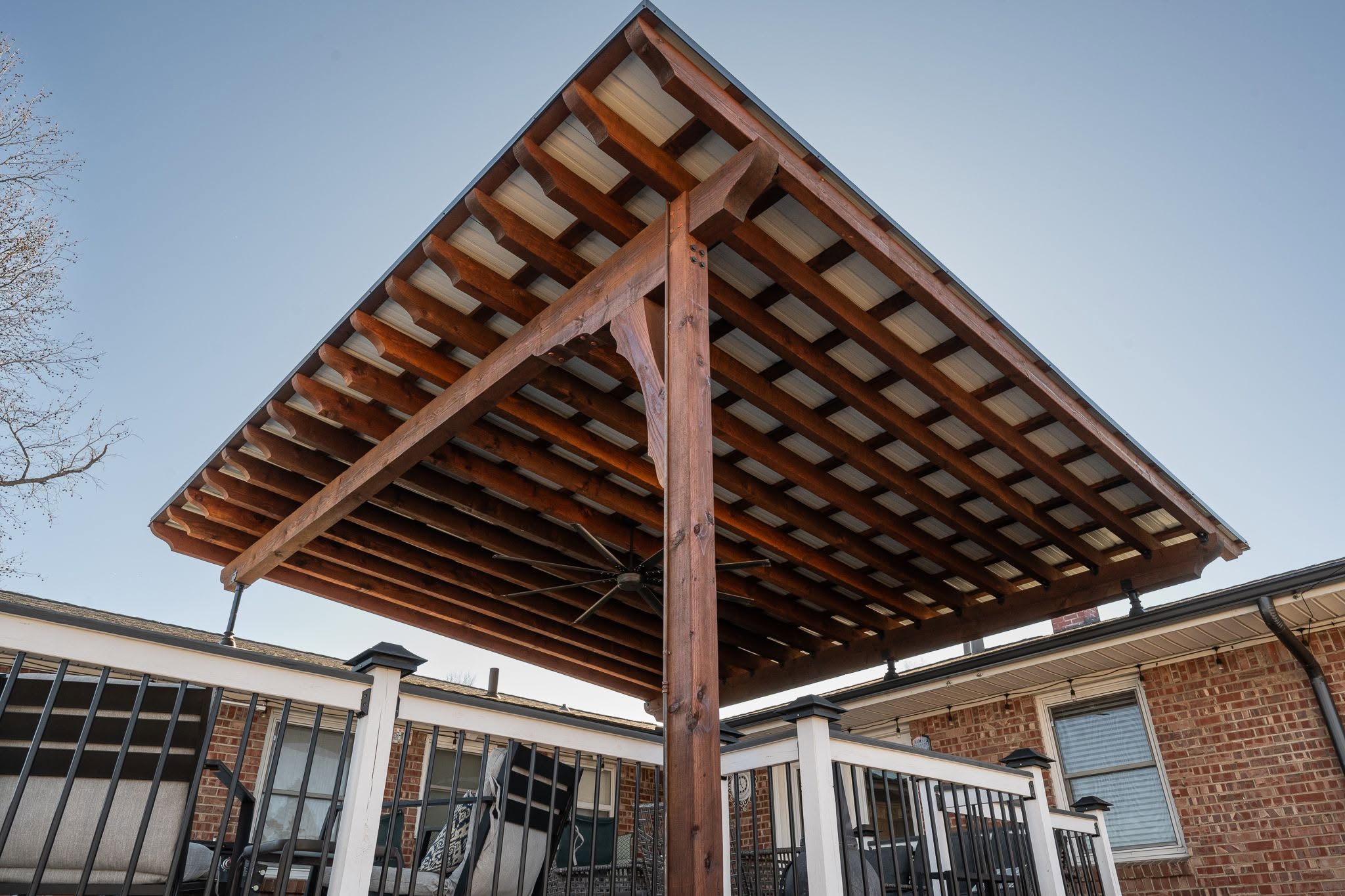 A wooden pergola with a metal roof covers a deck with outdoor furniture.