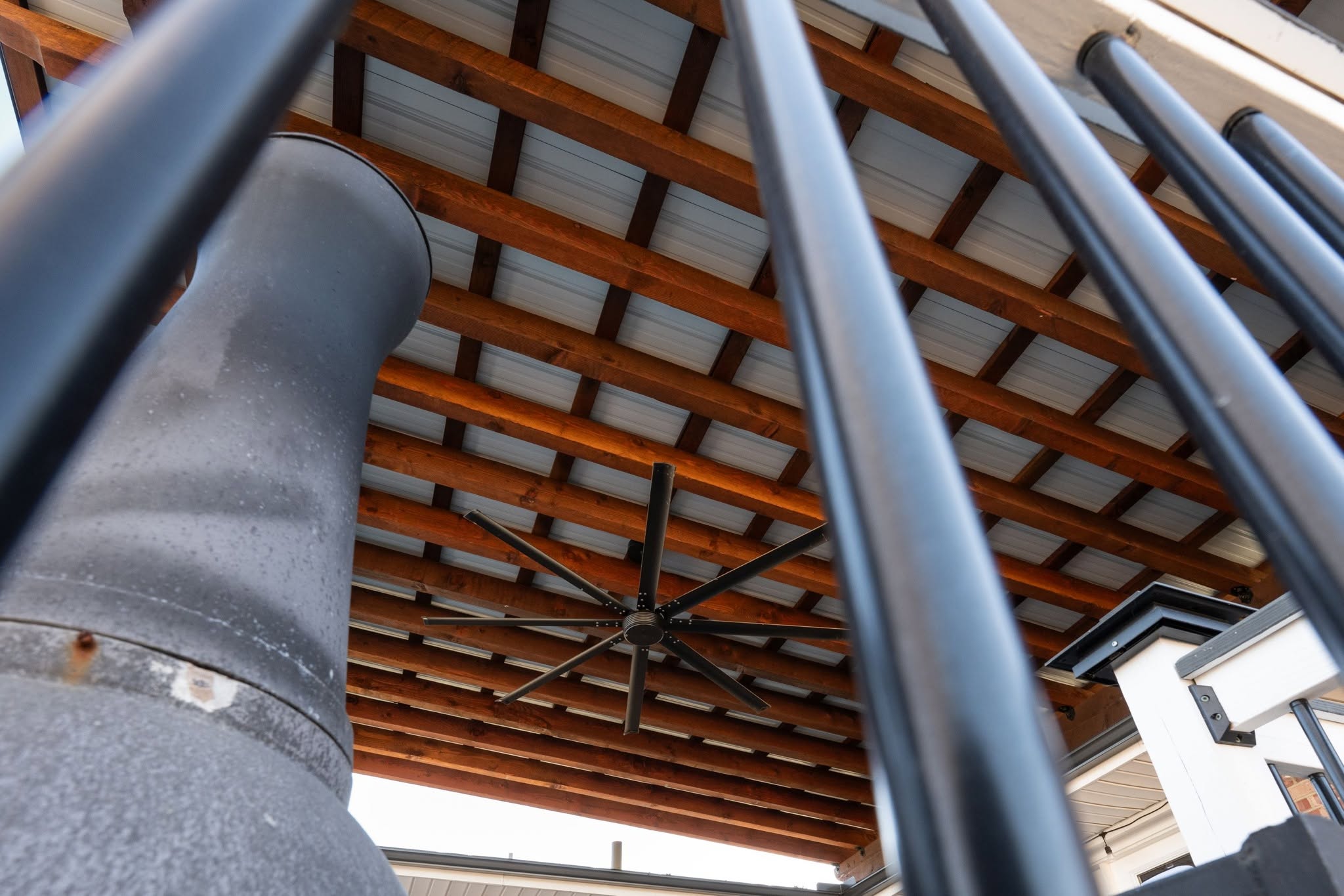 A large industrial fan hangs from a wooden beamed ceiling, partially obscured by black bars.