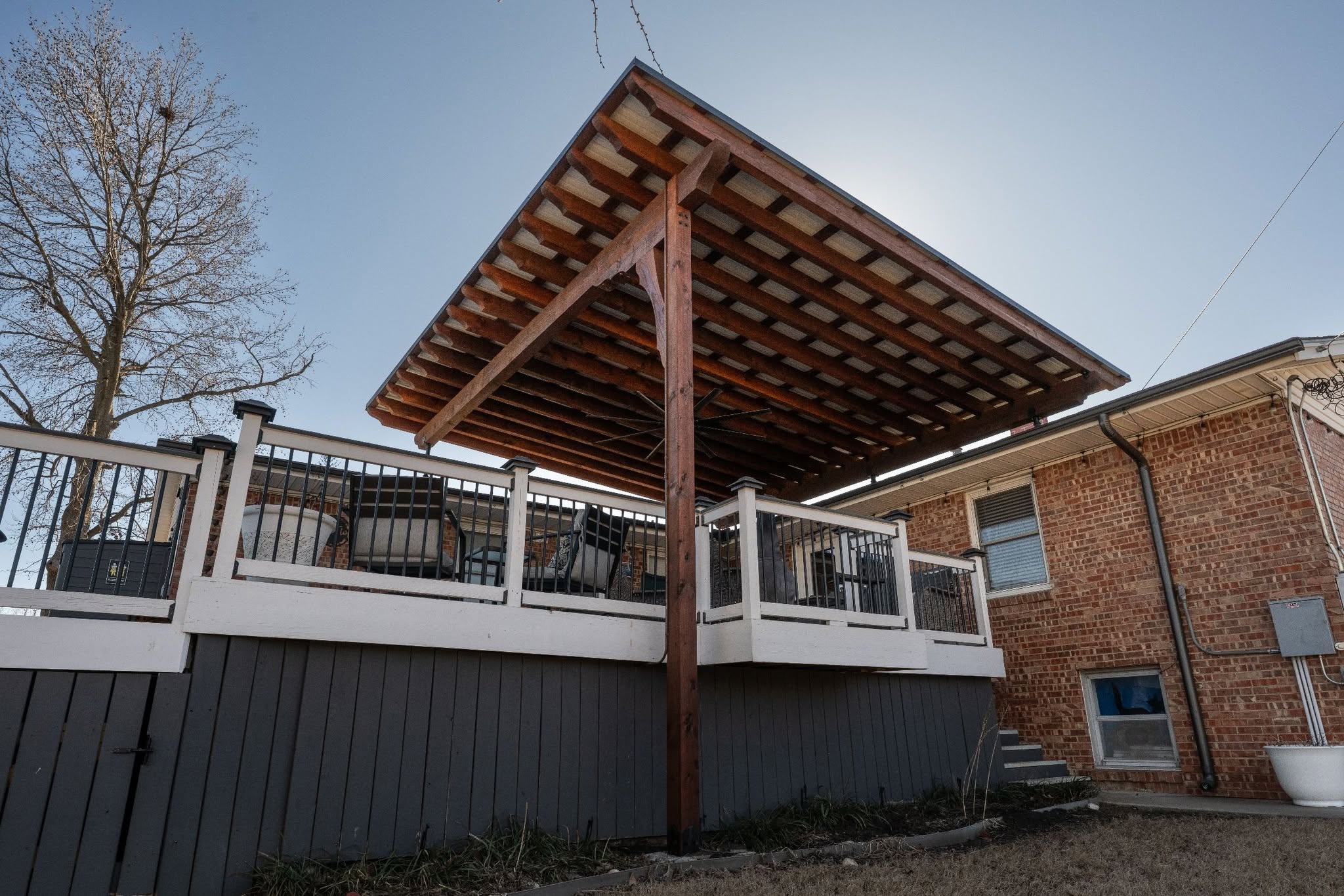 A wooden deck with a covered roof is attached to a brick house.