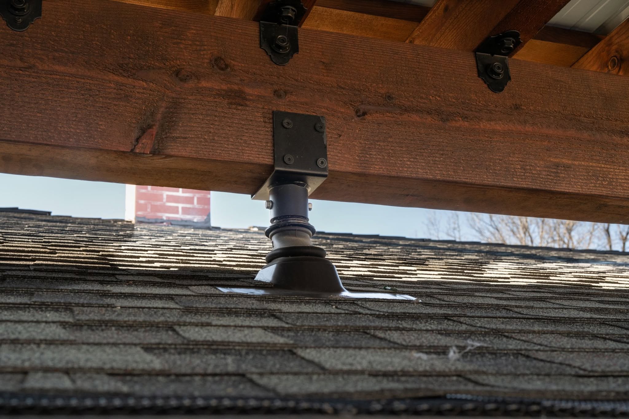 A close-up view of a wooden beam supported by a metal bracket over a shingled roof.