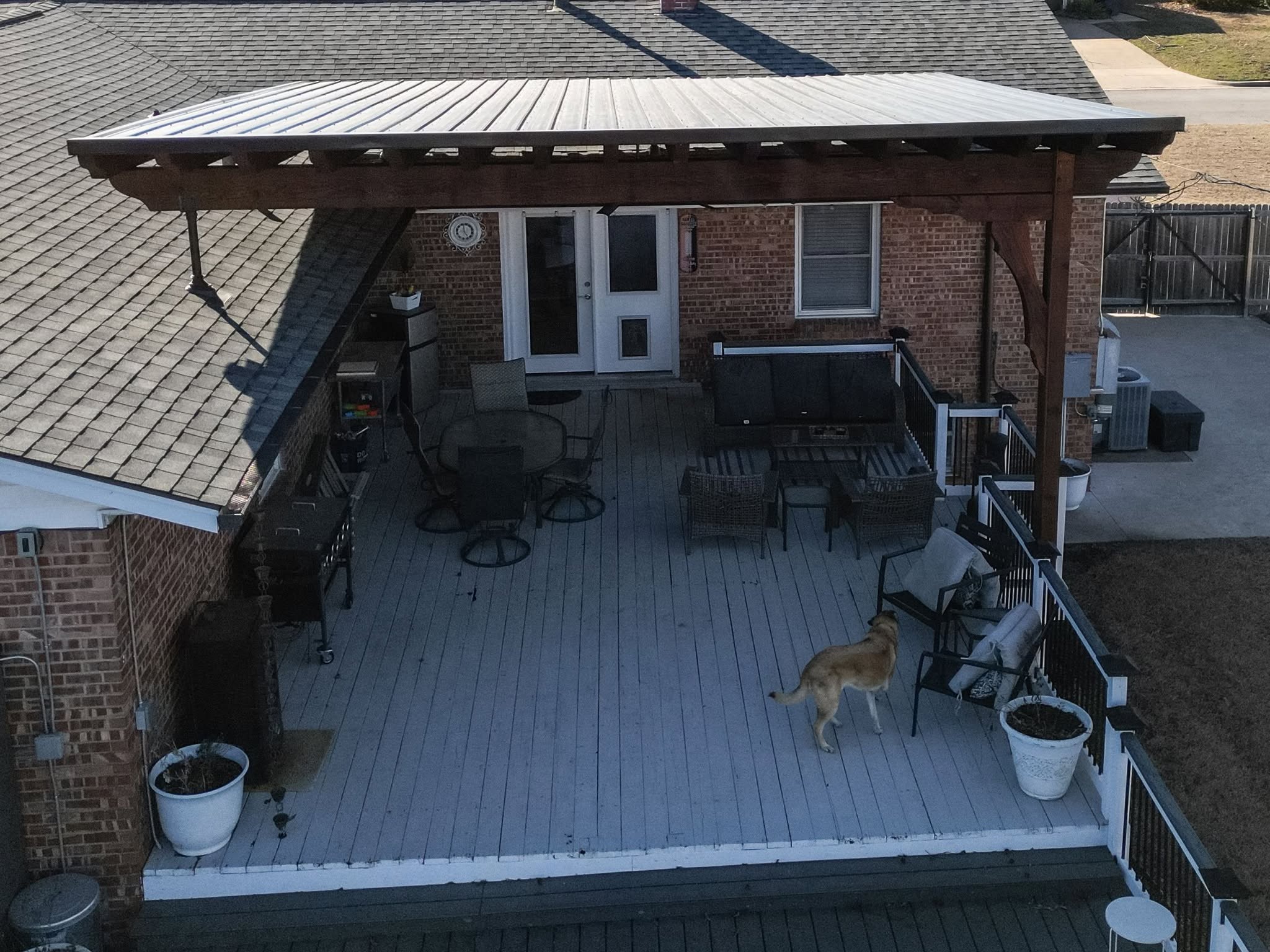A dog stands on a wooden deck with outdoor furniture and a covered patio.