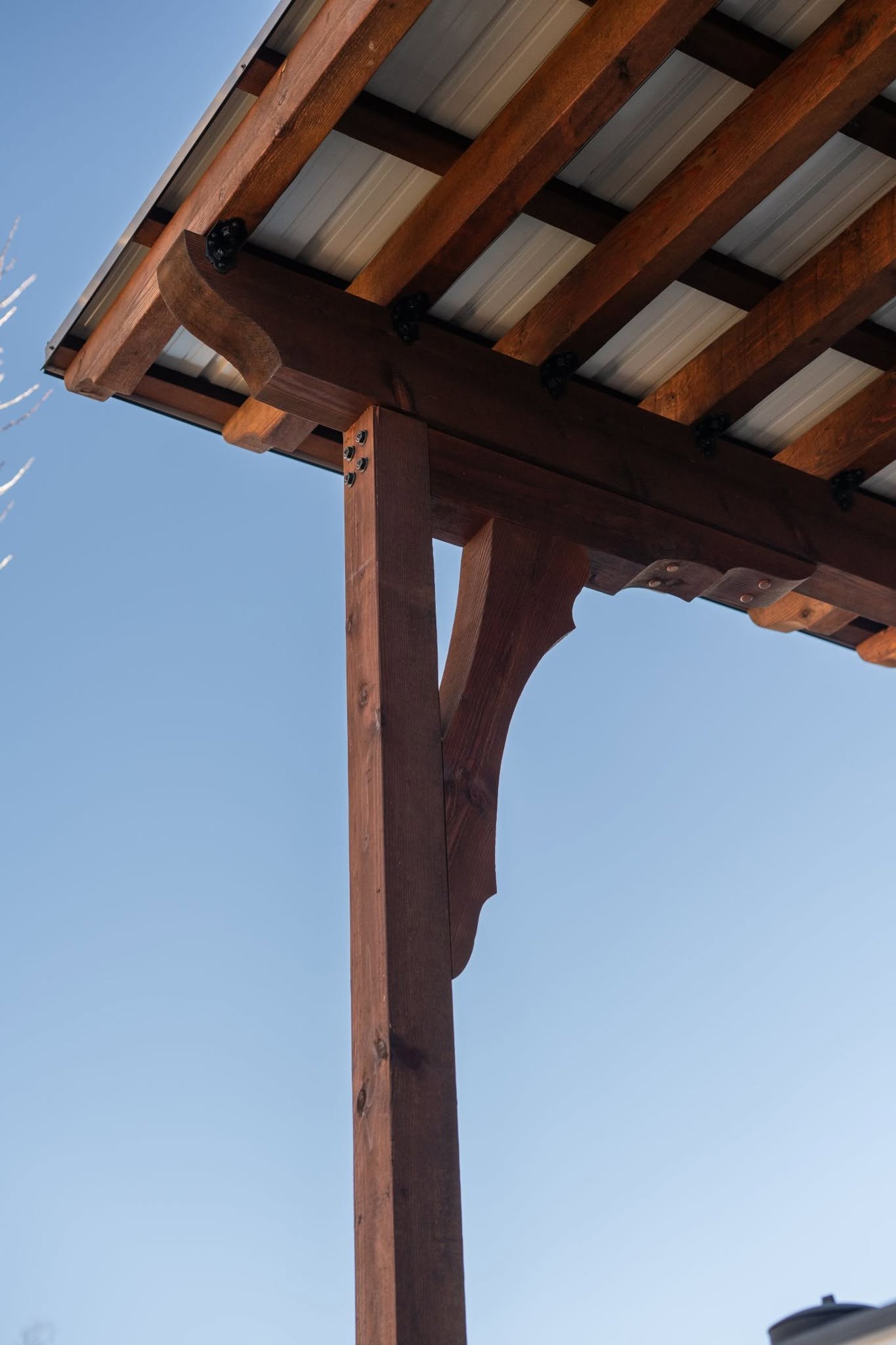 A wooden pergola with a metal roof is shown against a clear blue sky.