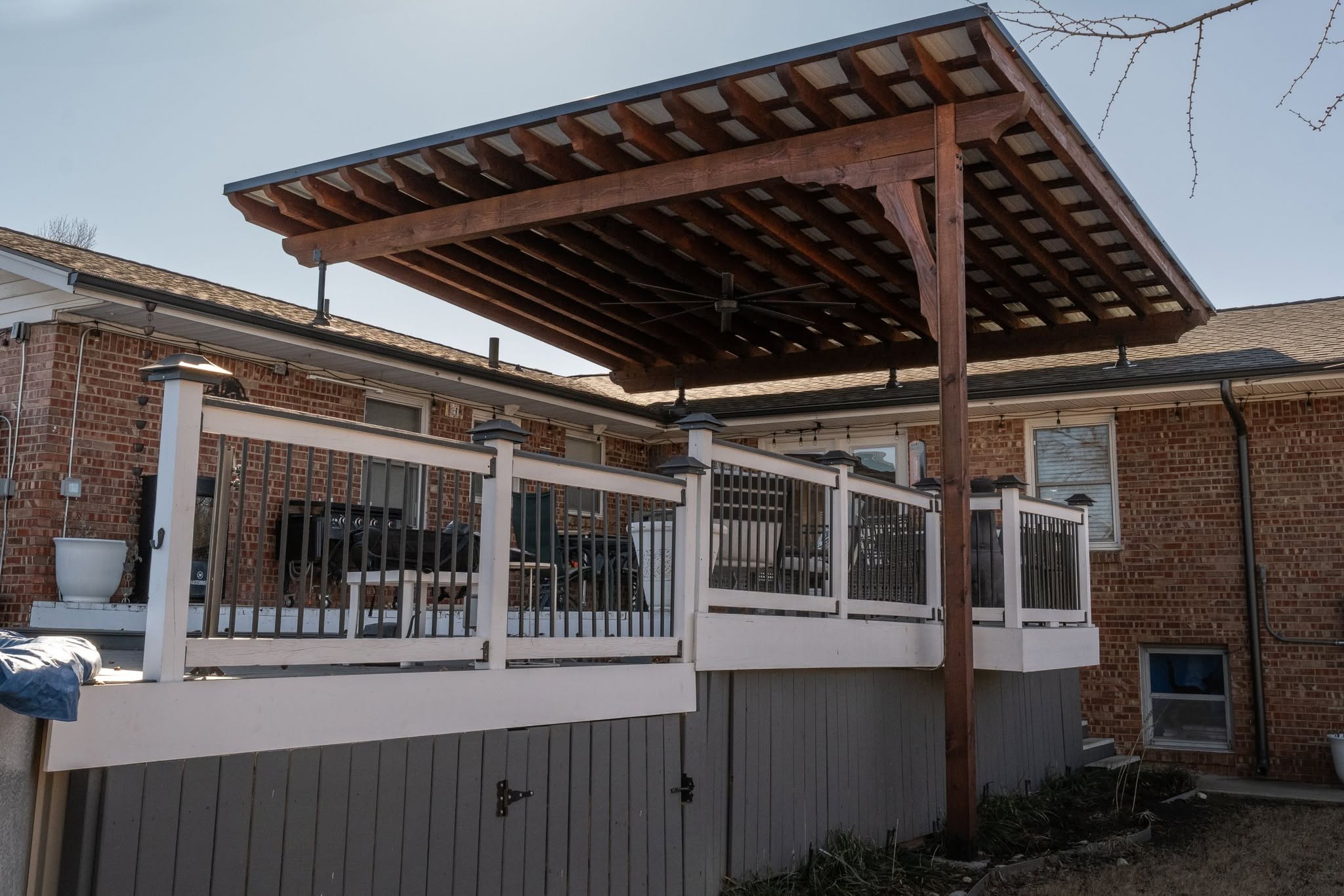 A covered deck with a fan is attached to a brick house.
