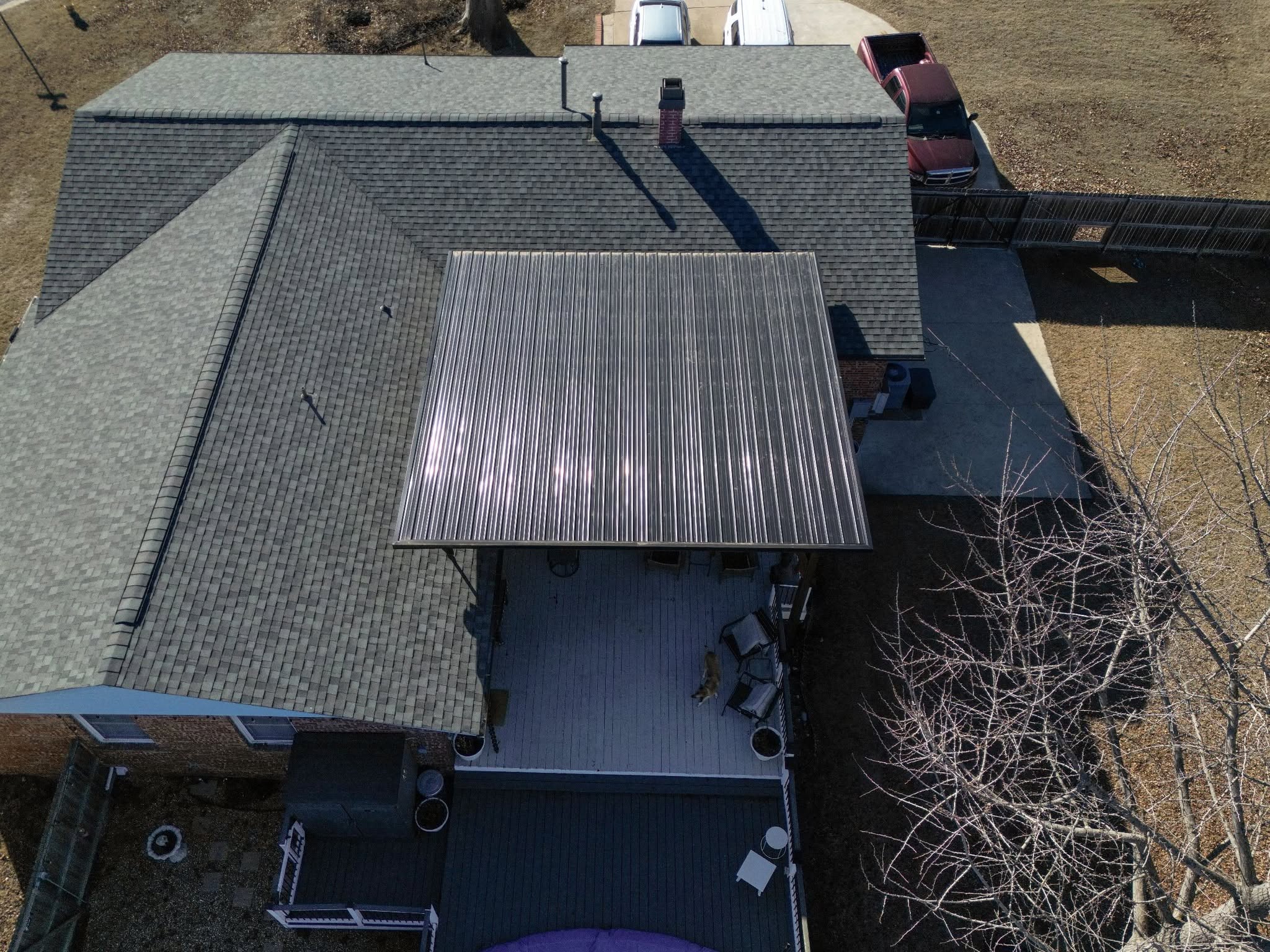 An aerial view shows a house with a metal-roofed patio, a deck, and a dog on the deck.