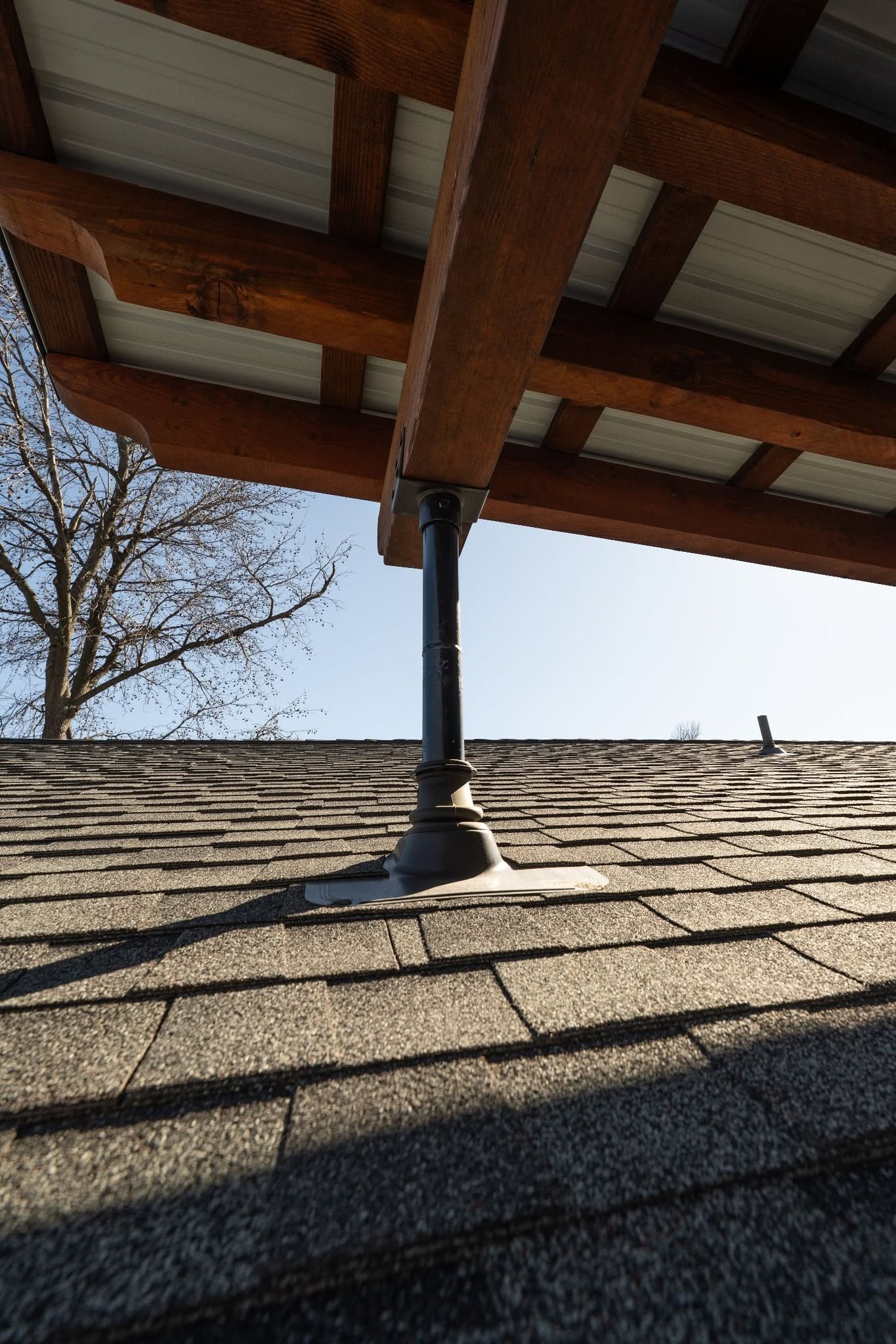 A dark metal support post anchors a wooden roof structure to a shingled roof.