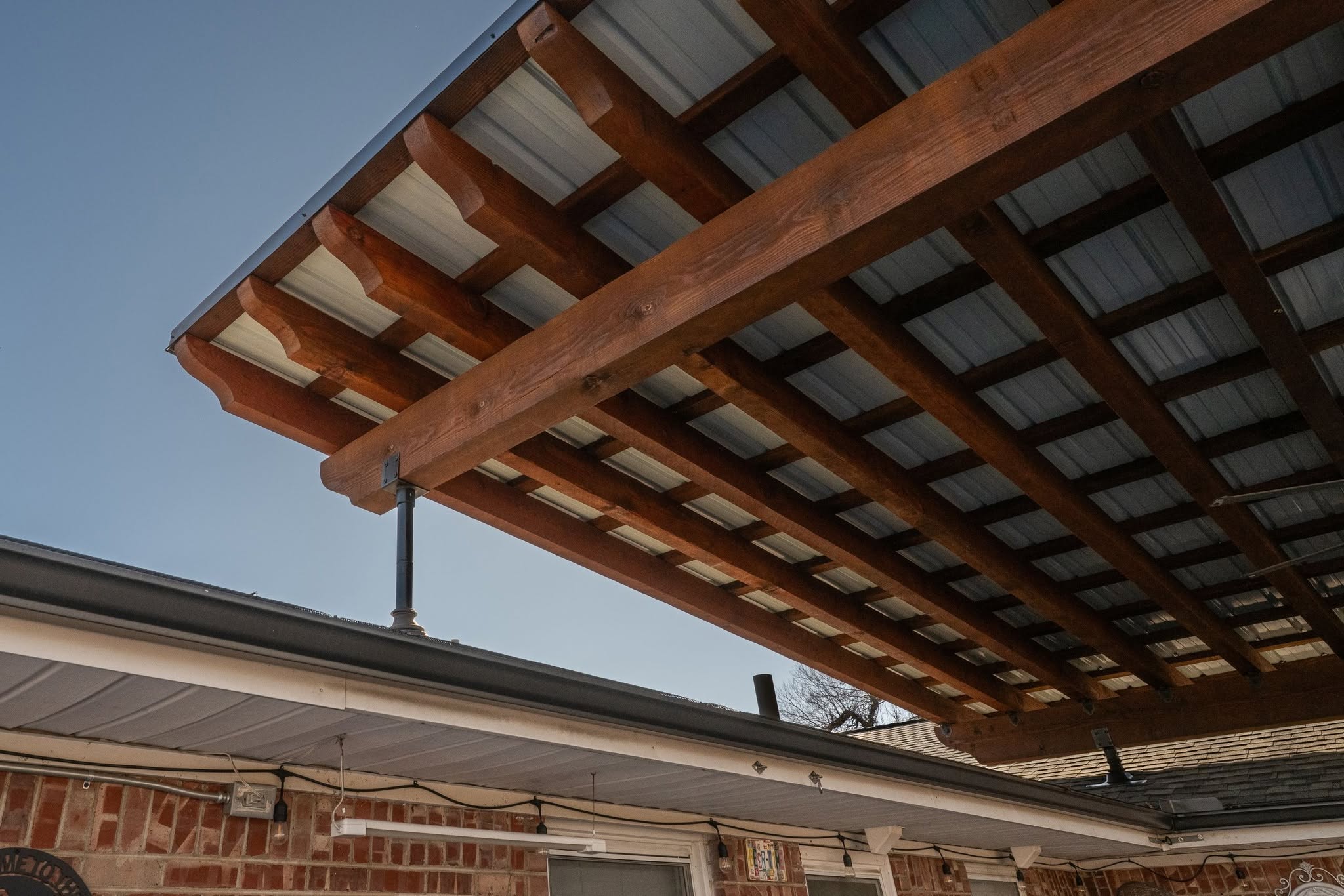 A wooden pergola with a metal roof extends over a brick house.