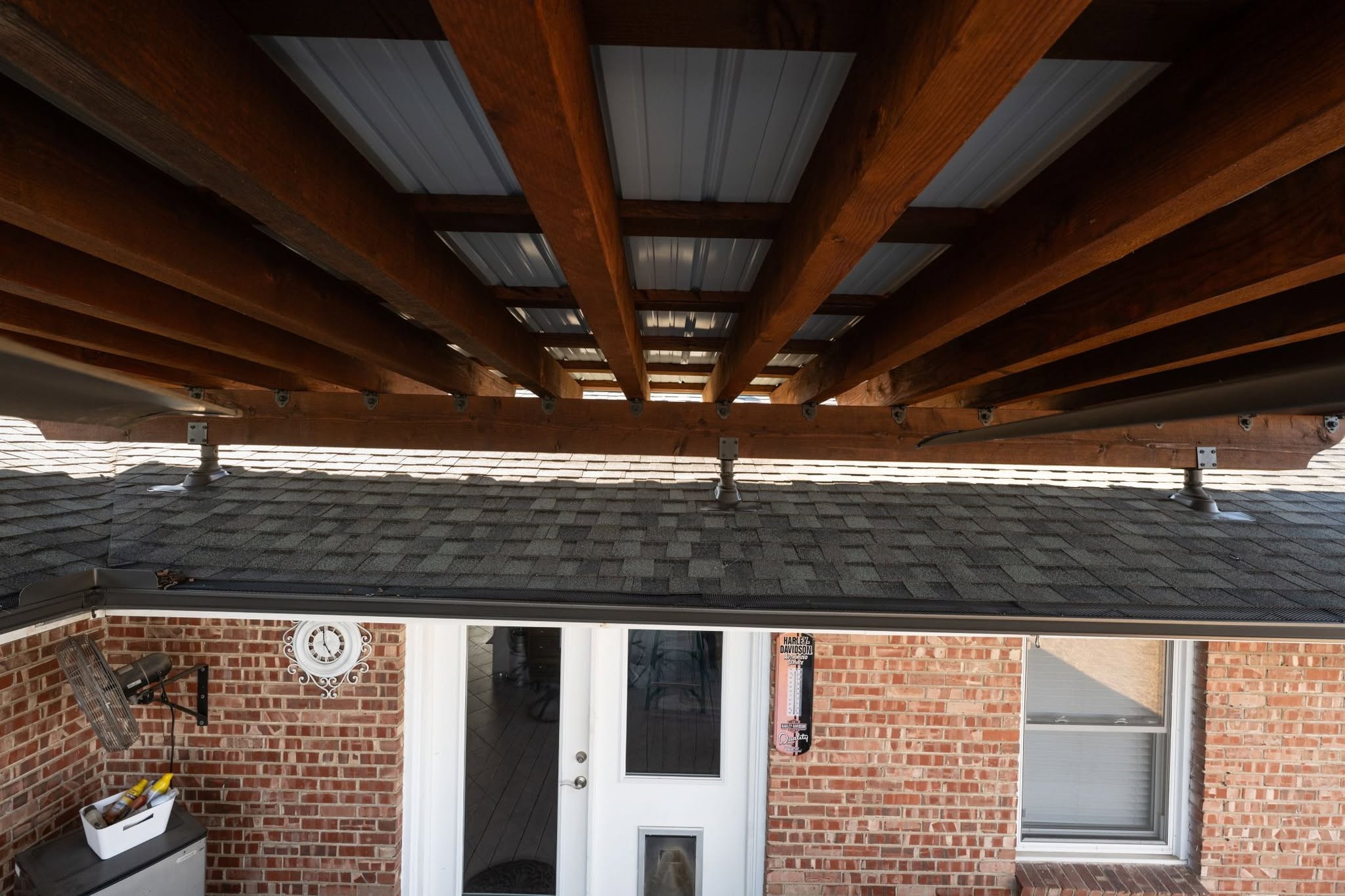 A covered patio with wooden beams above a brick building with a door and window.
