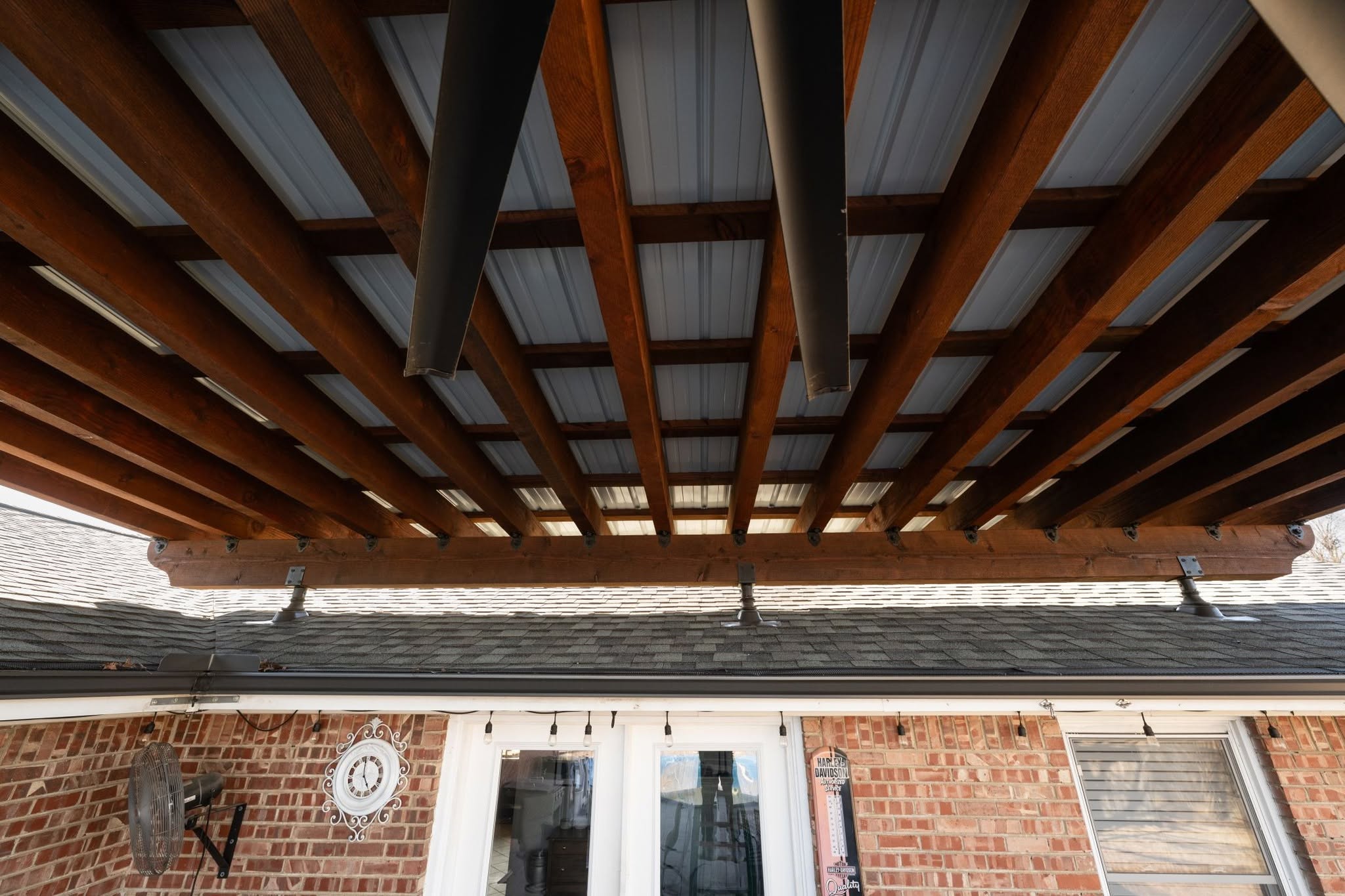 A covered patio with wooden beams and a metal roof over a brick house.