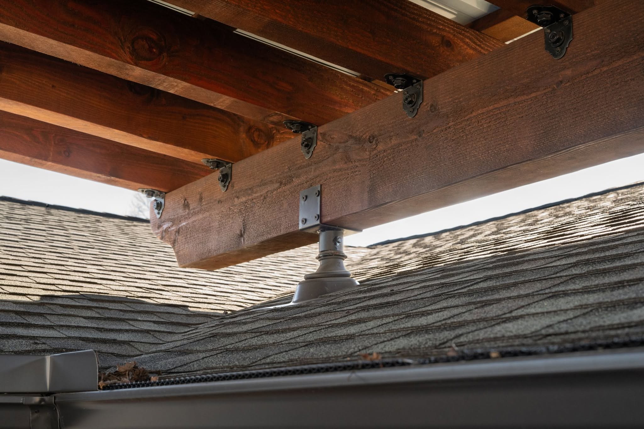 A wooden structure is supported by a metal post on a shingled roof.