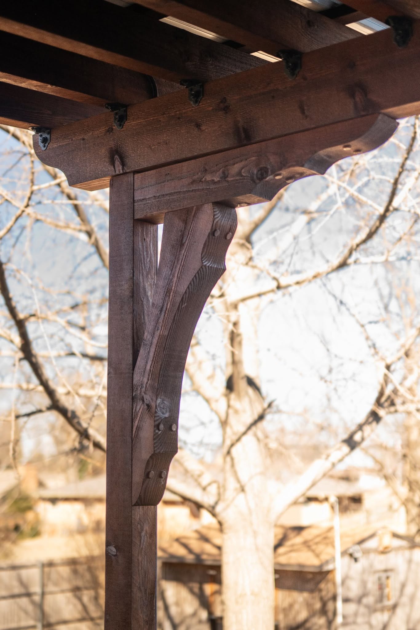 A wooden pergola support with decorative brackets is shown outdoors.