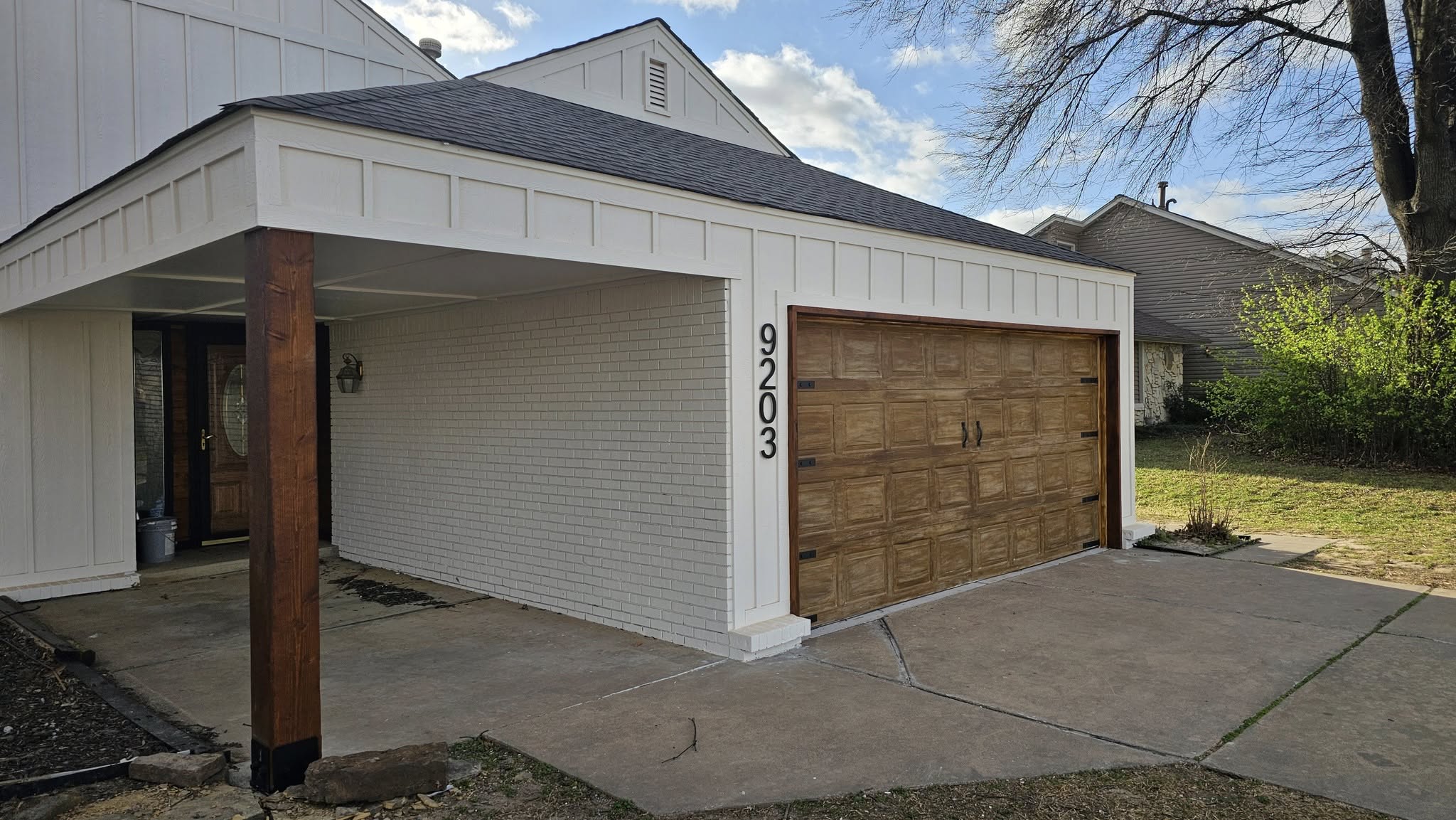 A house with a garage door and a covered entryway is shown in a suburban setting.