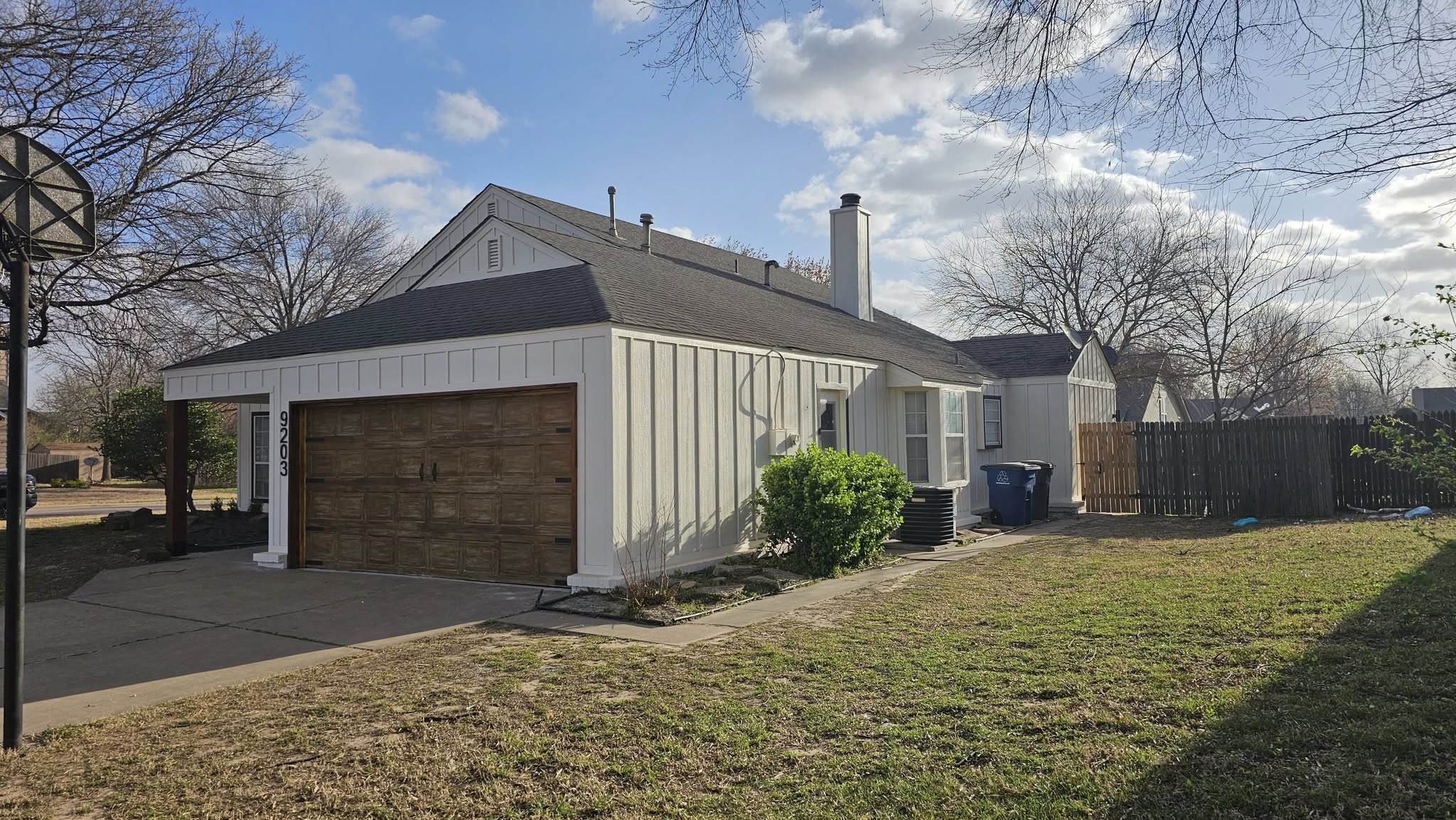 A white house with a brown garage door is shown in a suburban yard on a sunny day.