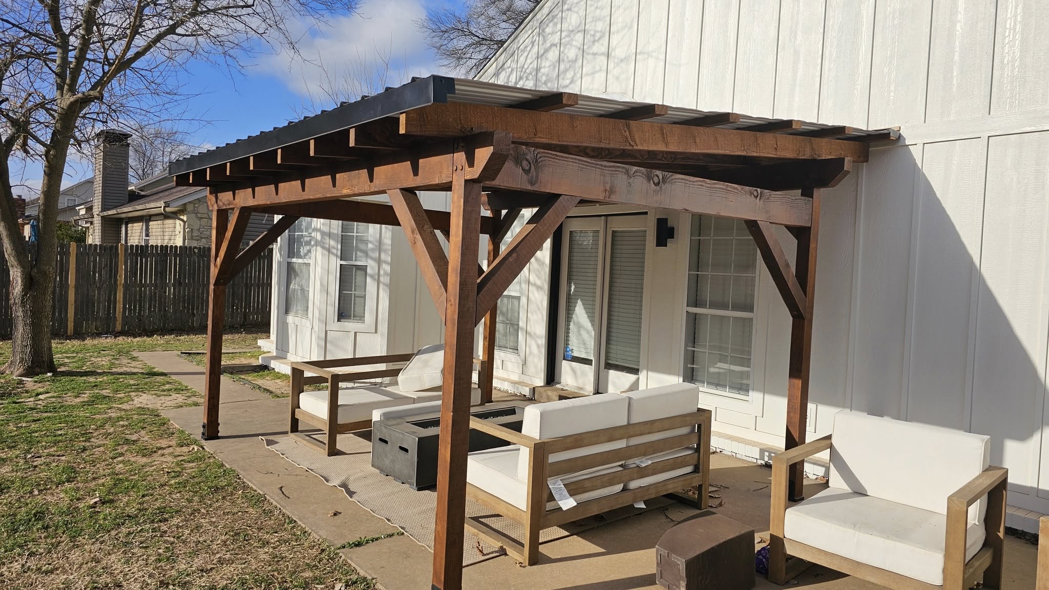 A backyard patio with wooden furniture and a pergola is shown.