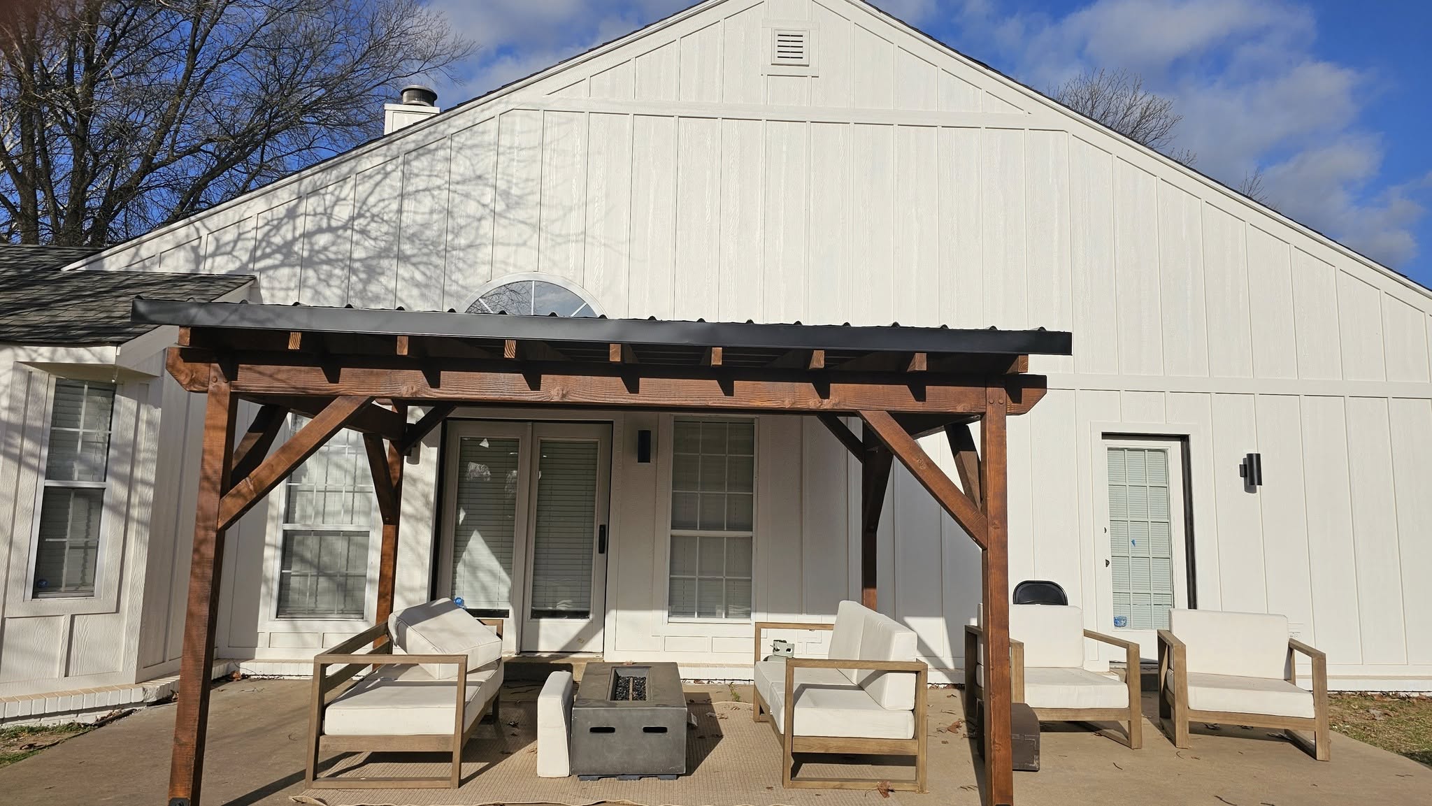 A white modern farmhouse with a wooden pergola and outdoor seating on a patio.