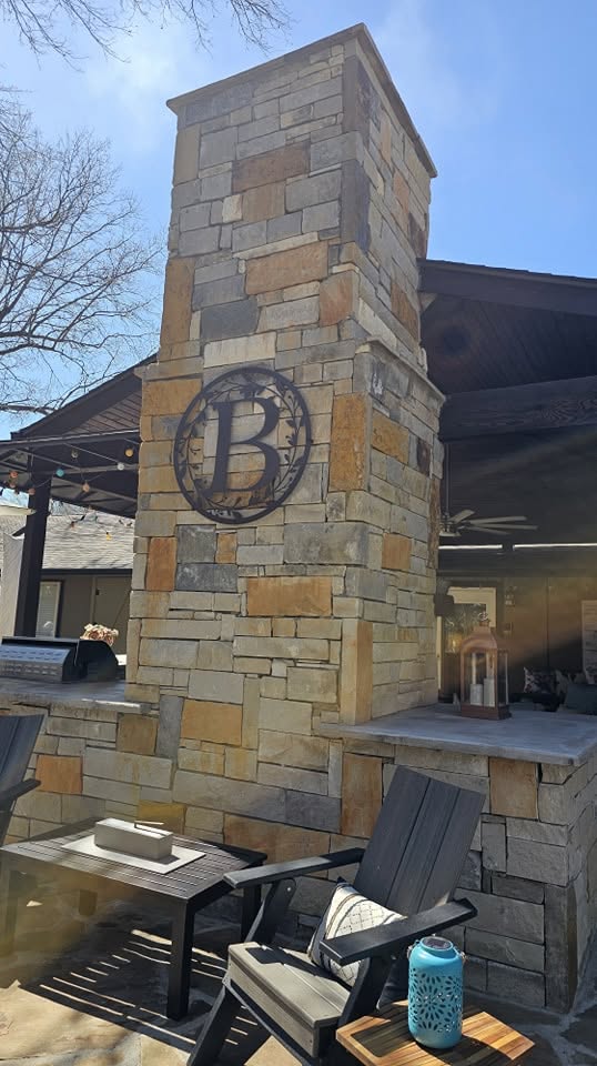 A stone outdoor fireplace with a monogram and seating area is shown on a patio.