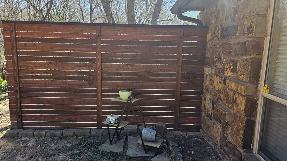 A wooden fence stands next to a stone wall with decorative planters in a yard.