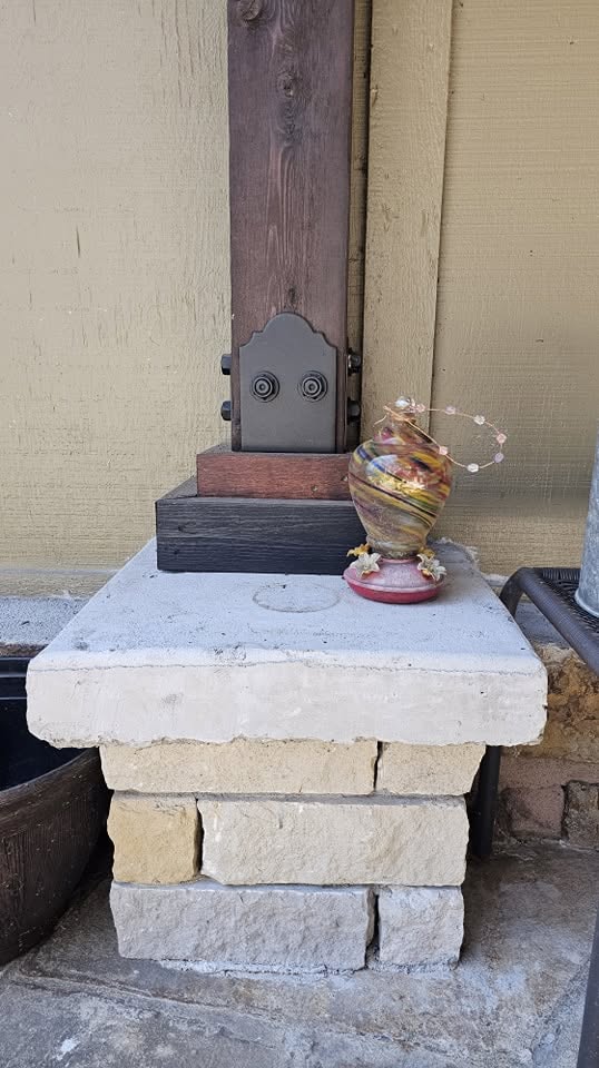 A decorative vase sits on a stone pedestal next to a wooden post.