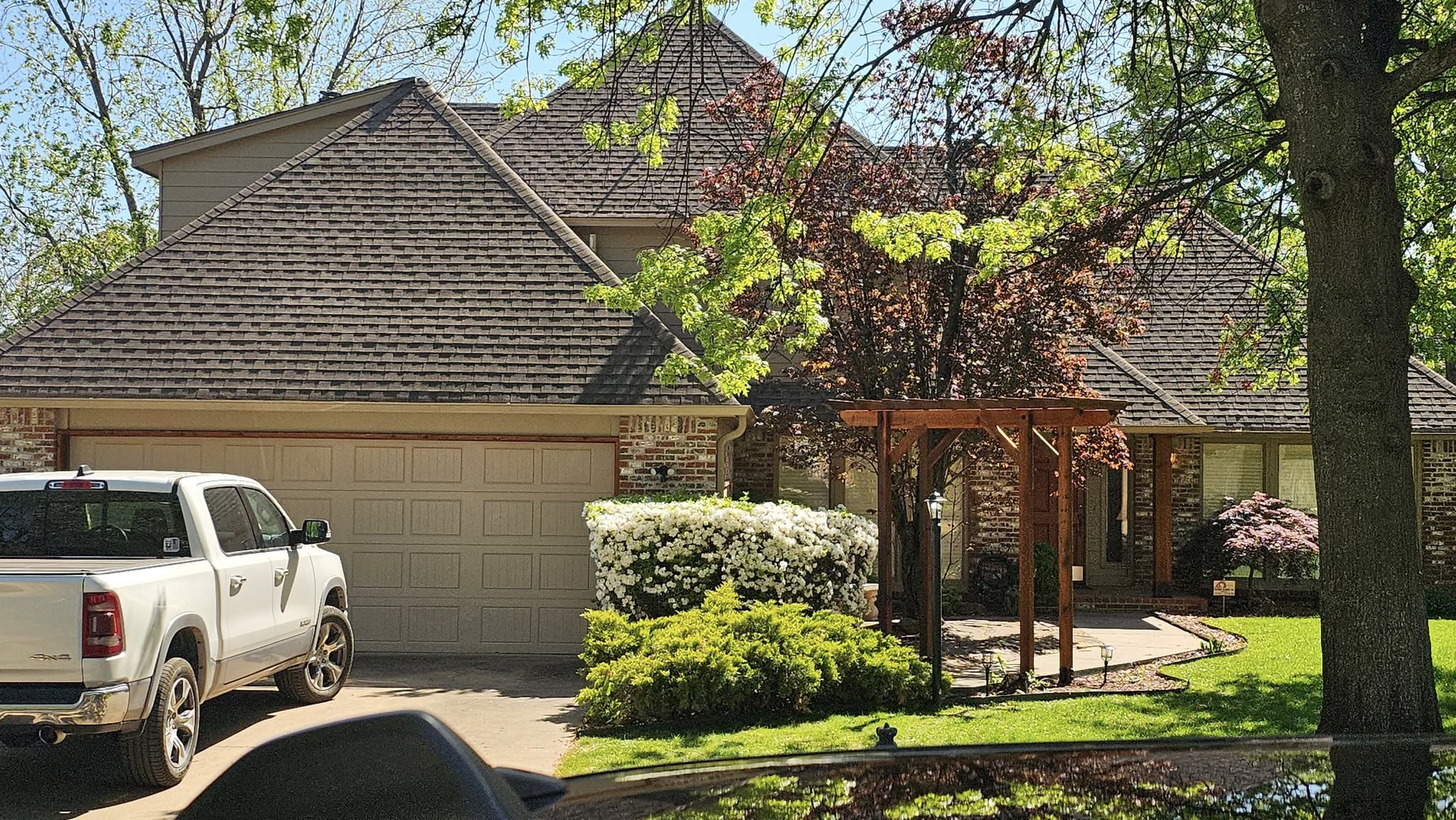 A white truck is parked in front of a brick house with a large white flowering bush.