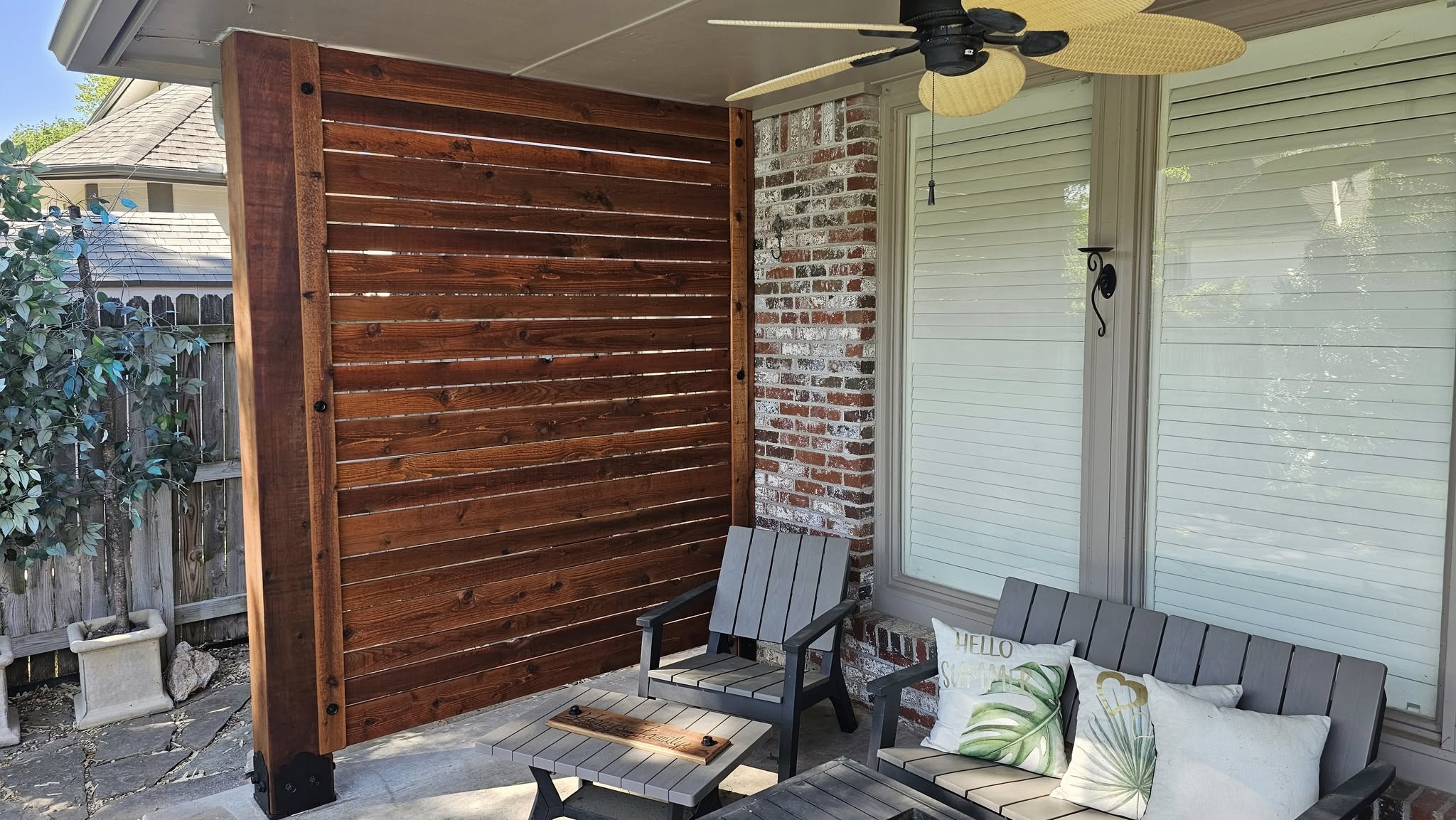 An outdoor patio with furniture, a wooden privacy screen, and a ceiling fan.