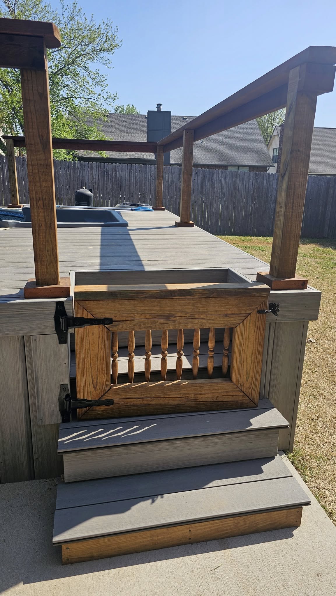 A wooden gate on a composite deck with stairs leads to a backyard.