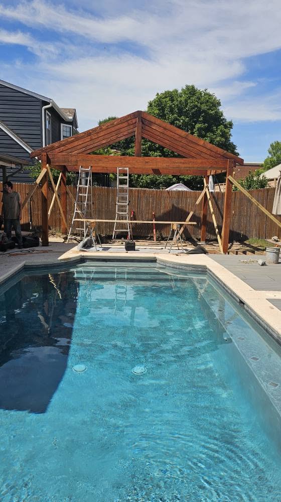 A wooden pergola is under construction next to a swimming pool in a backyard.